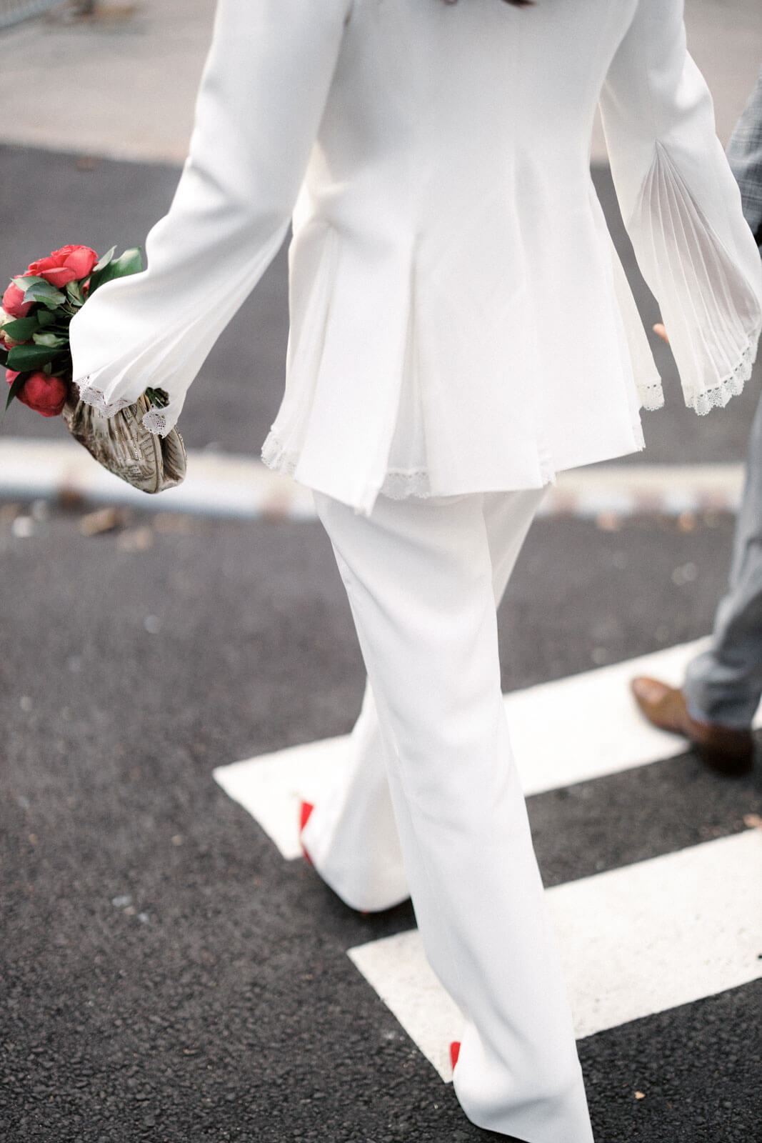 Half body shot of the bride wearing red shoes, crossing the pedestrian lane, while holding her red flower bouquet. Image by Jenny Fu Studio
