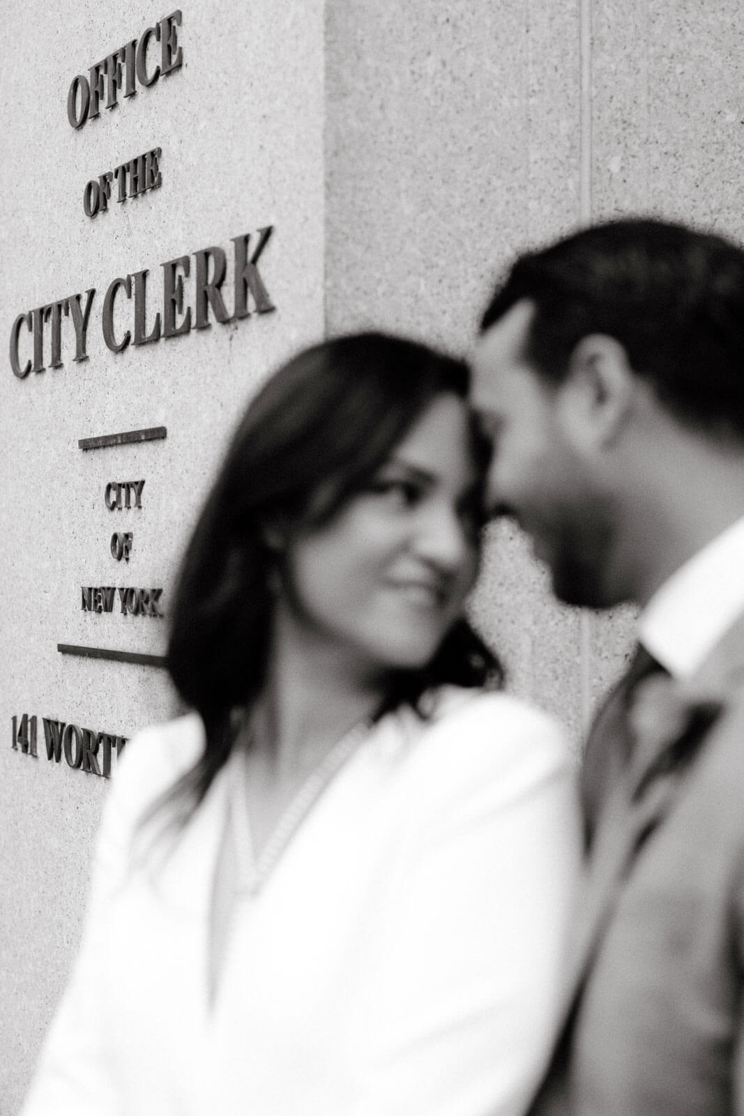 Black and white photo of the bride and the groom in front of NYC Office of the City Clerk.
