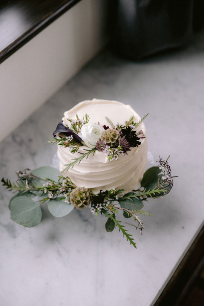 Simple but beautiful small, white wedding cake with white, violet and light brown flowers with green leaves. Image by Jenny Fu Studio