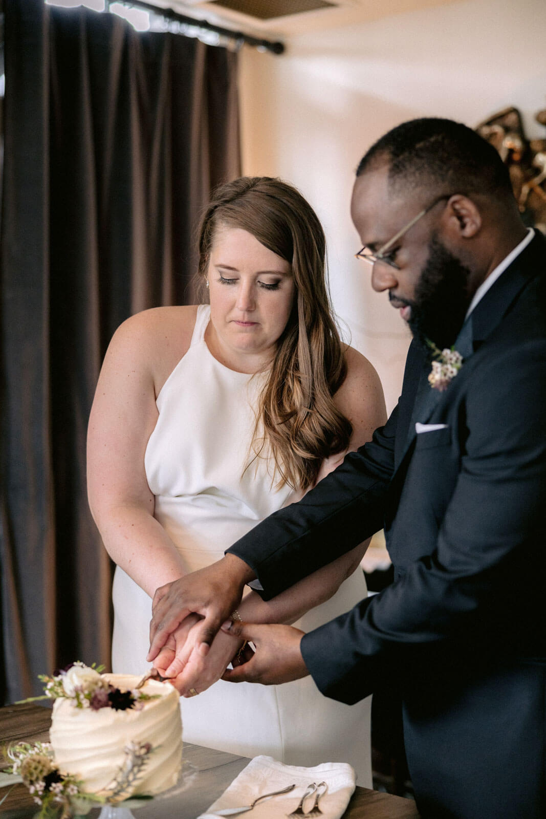 The newlyweds are cutting their small, white wedding cake in New York City. Image by Jenny Fu Studio
