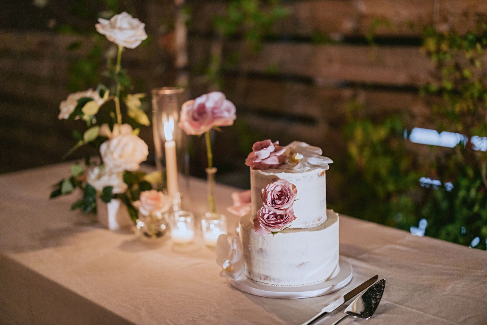 Pretty, two-tiered small, white wedding cake with pink flowers on a table with candles, white and pink flowers. Image by Jenny Fu Studio 
