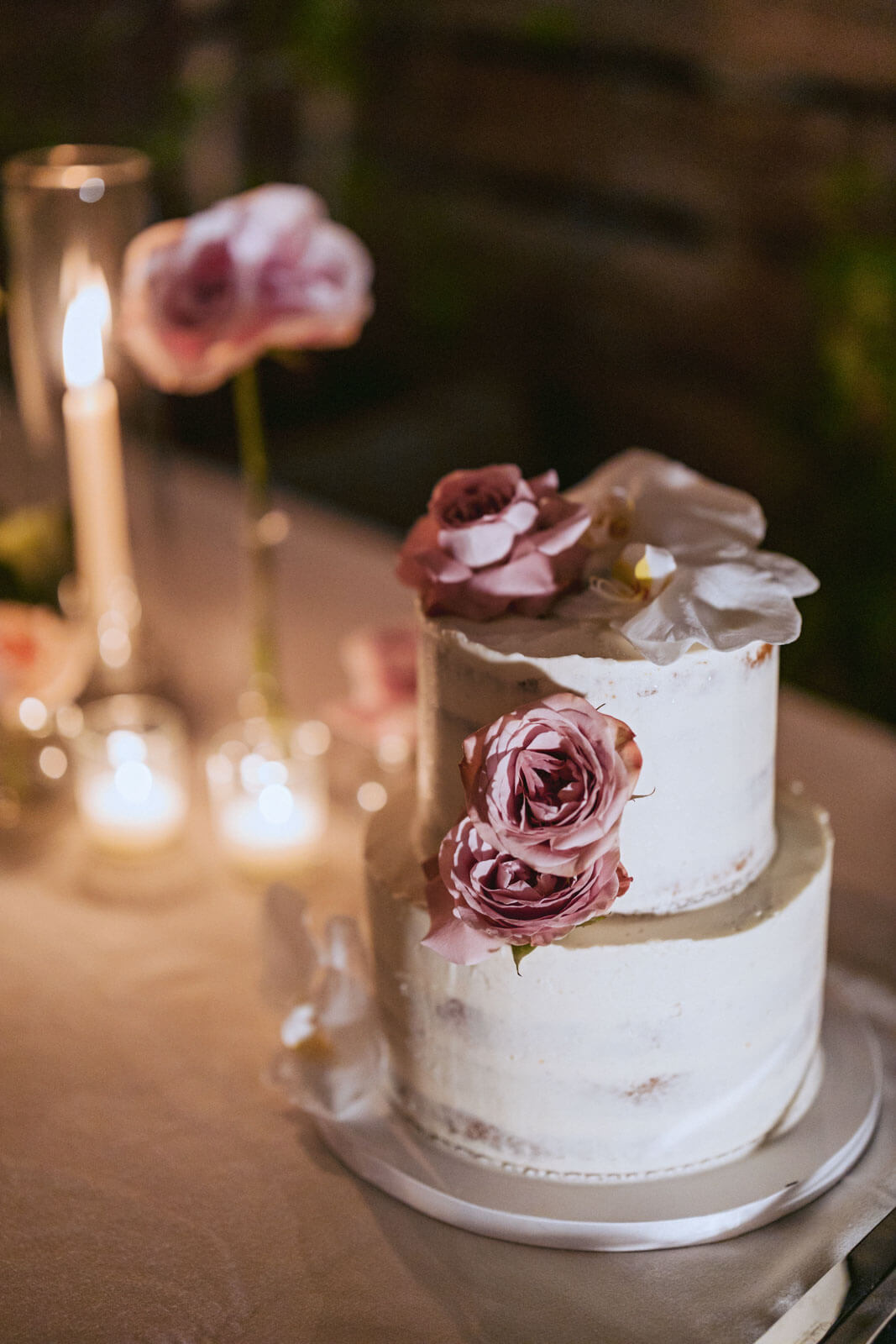 Pretty, two-tiered small, white wedding cake with pink flowers on a table with candles, white and pink flowers. Image by Jenny Fu Studio