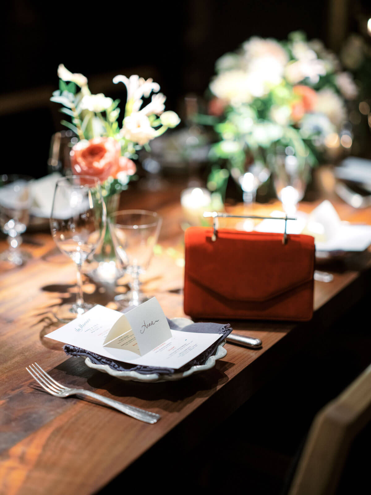 A red clutch is placed on a table with beautiful flower centerpieces. Love month wedding image by Jenny Fu Studio