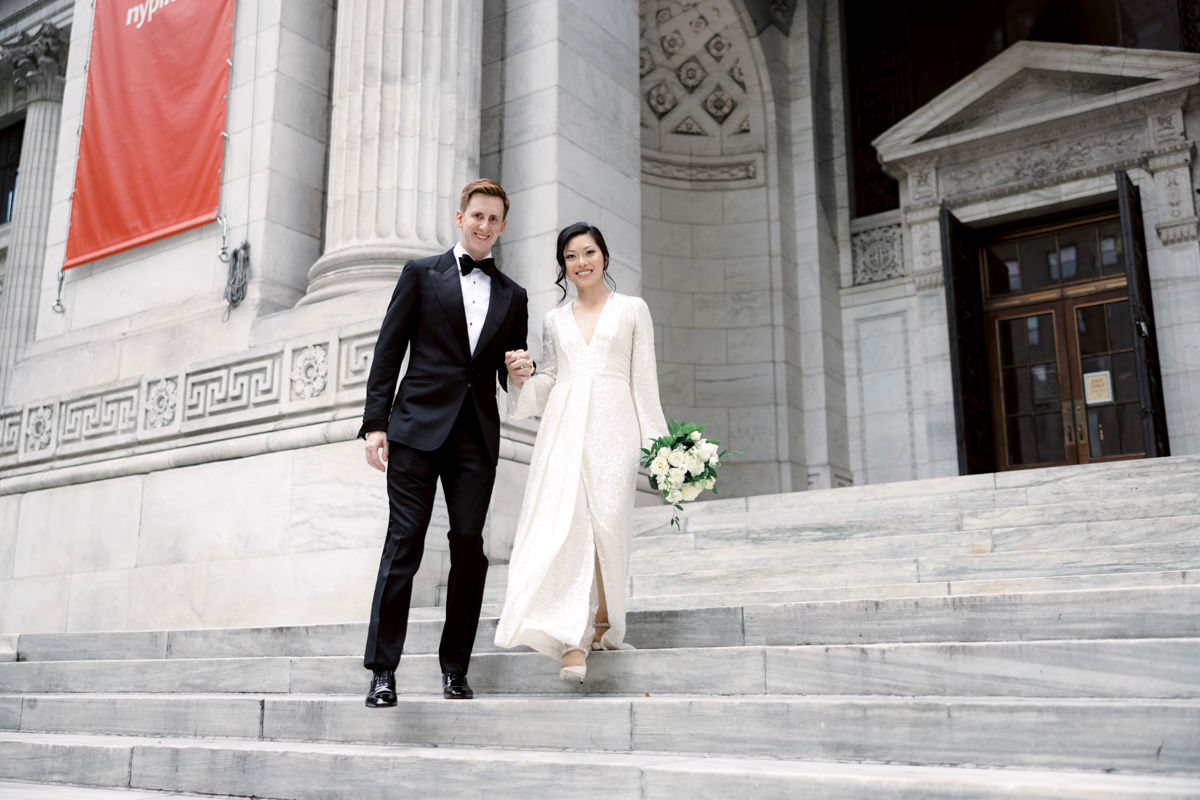 The bride and the groom are happily standing on the grand entrance staircase of the NYPL. Image by Jenny Fu Studio