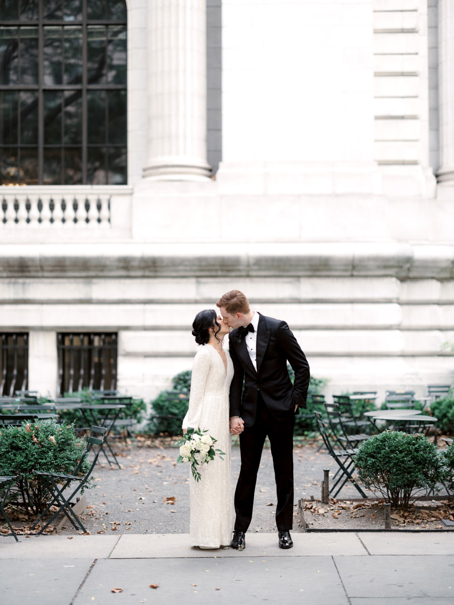 The bride and groom are kissing outside the New York Public Library. Image by Jenny Fu Studio