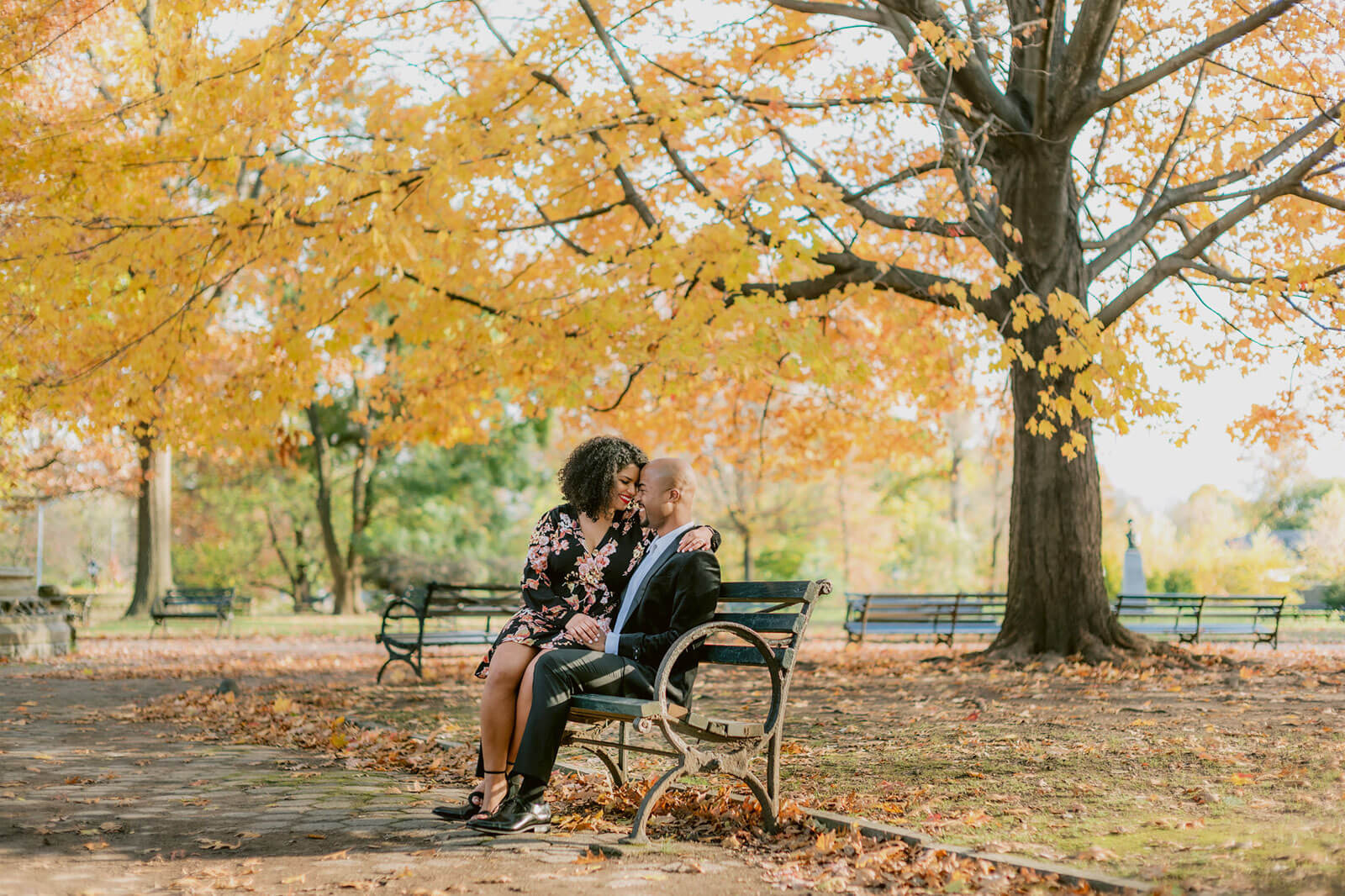 The engaged couple is happily sitting on a park bench in Brooklyn. NYC Christmas Engagement Photos by Jenny Fu Studio  