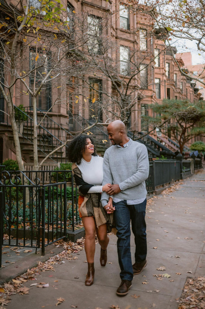 The engaged couple is happily walking along a Brooklyn road. NYC Christmas Engagement Photos by Jenny Fu Studio