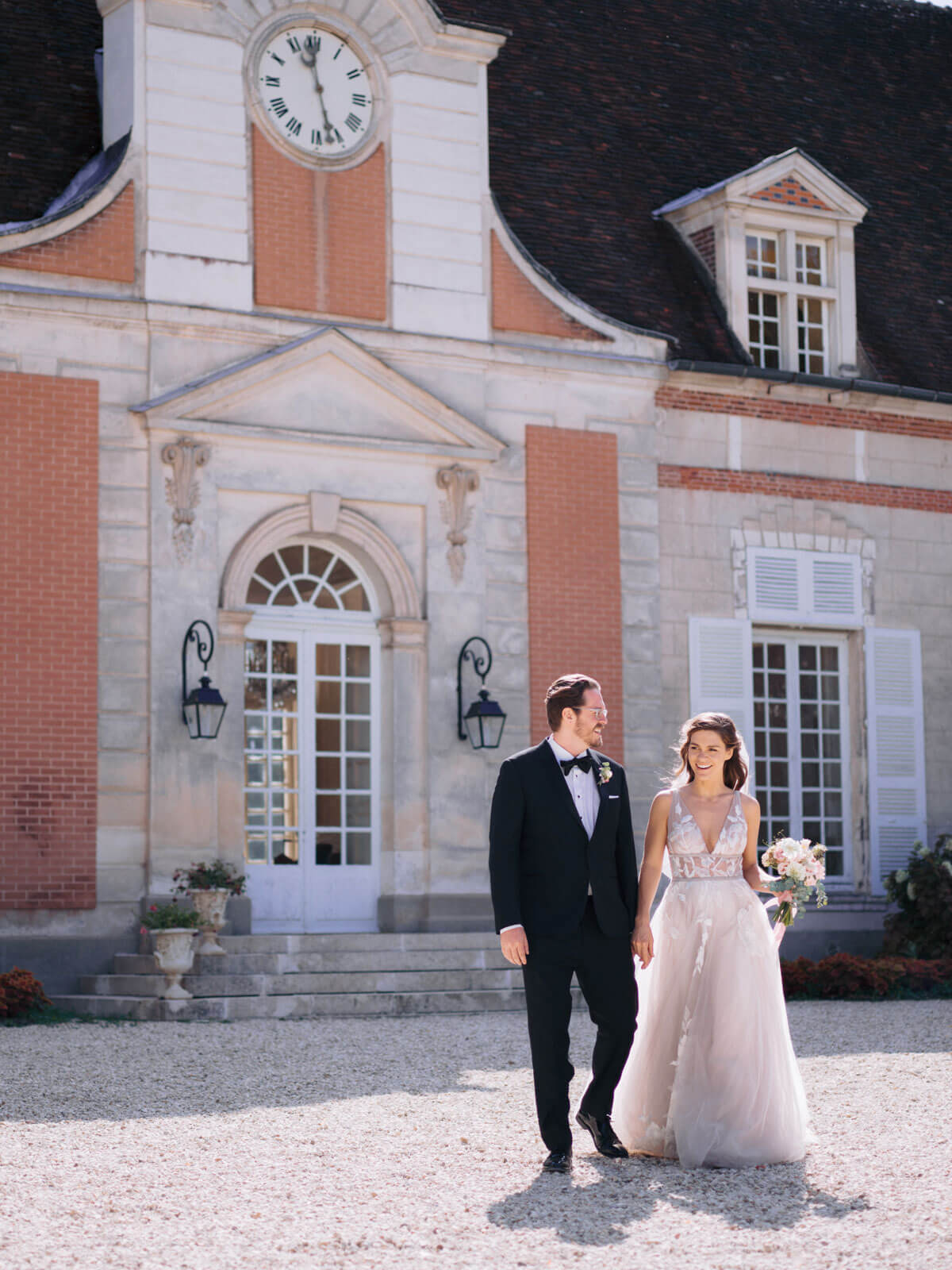 The bride and groom are walking in front of a chateau in France. Image by Destination Wedding Photographer Jenny Fu