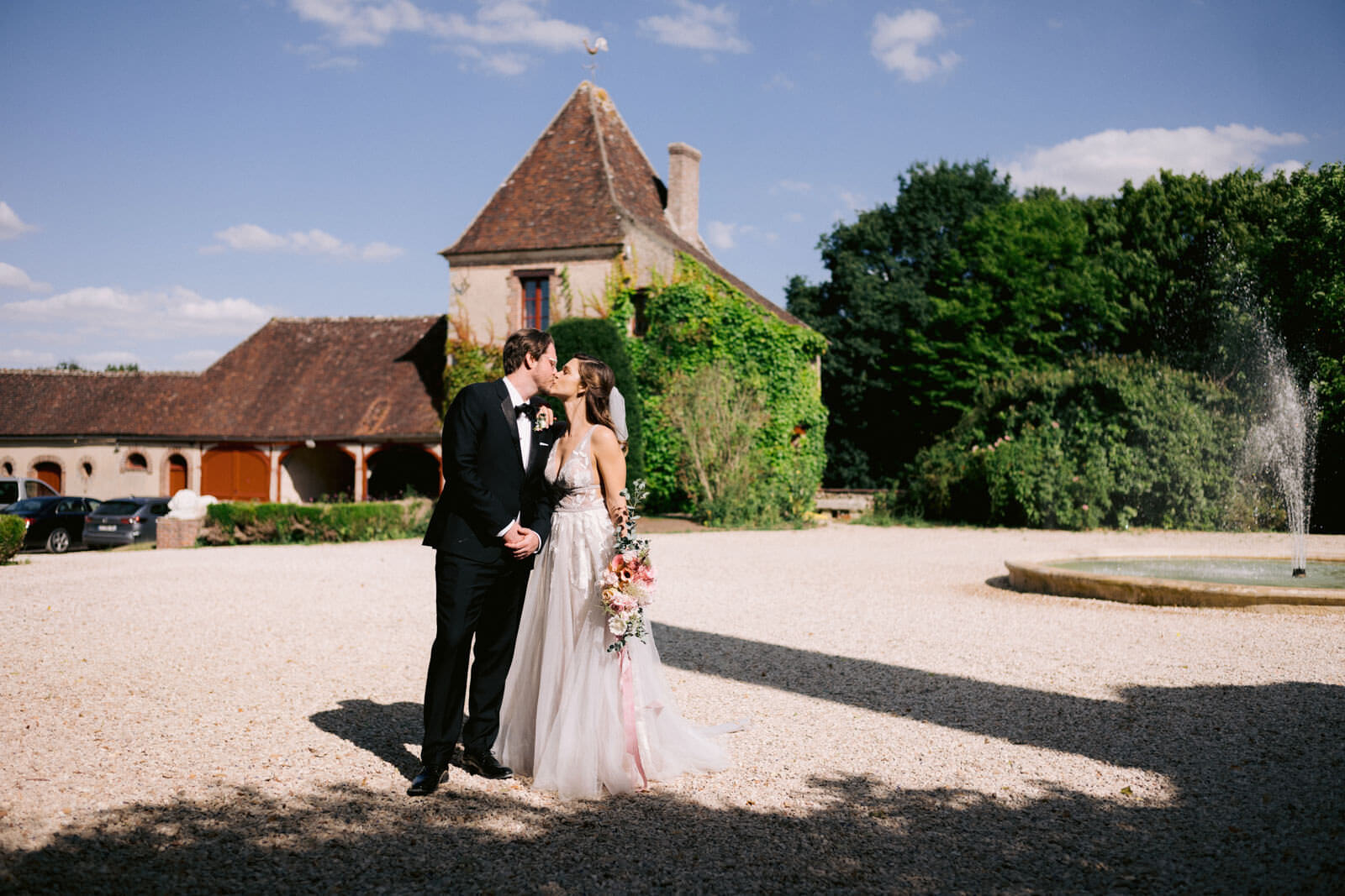 The bride and groom are kissing outside a chateau. Outdoor wedding destination image by Jenny Fu Studio