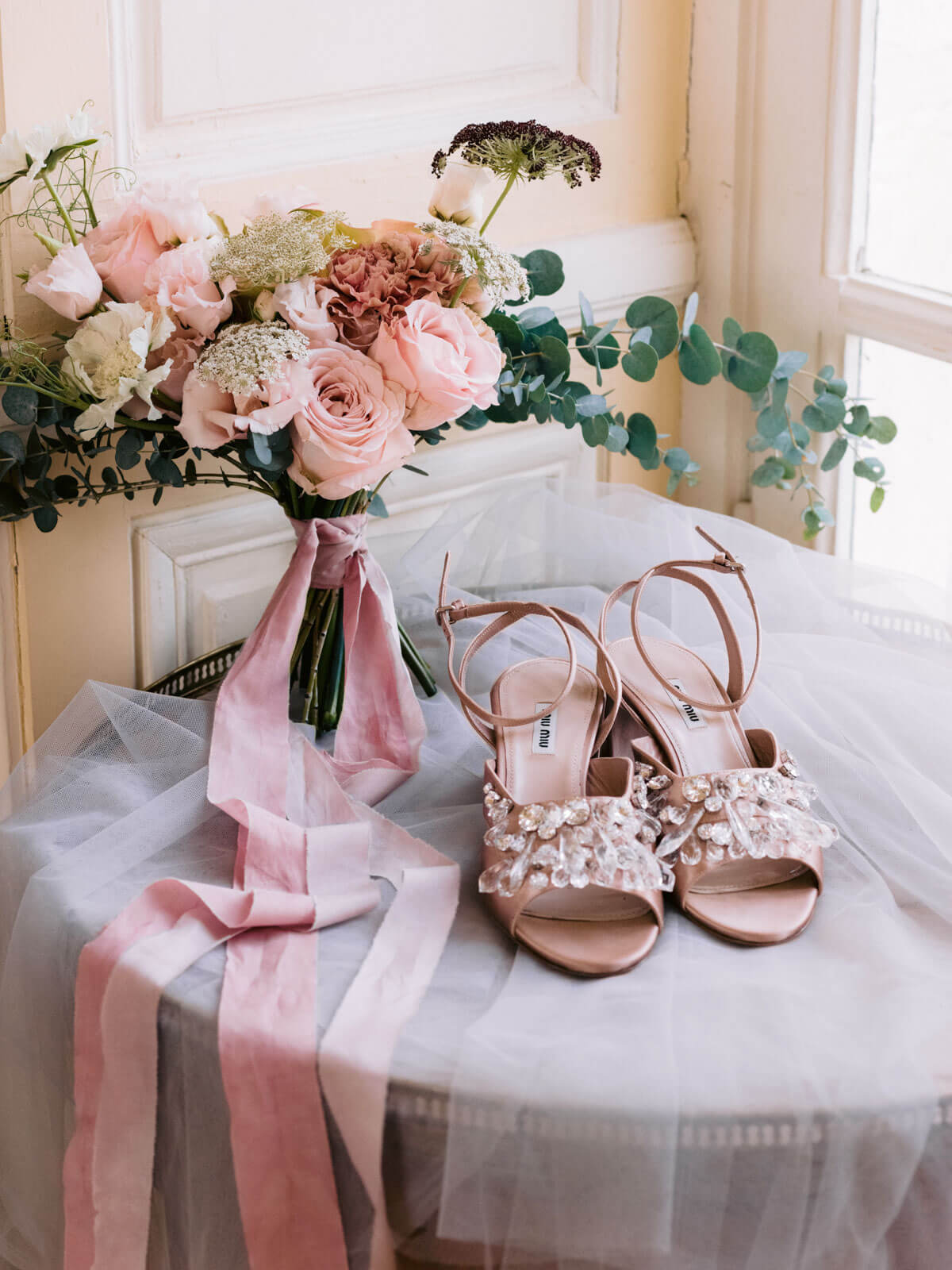 The bride's flower bouquet and her wedding shoes placed on a table. Outdoor wedding destination image by Jenny Fu Studio
