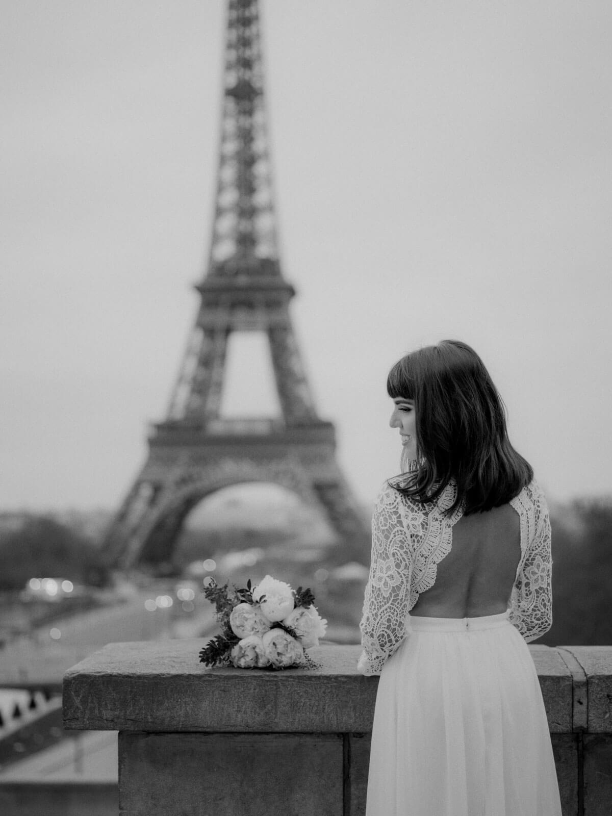 The bride is standing on a terrace overlooking the Eiffel Tower. Destination wedding image by Jenny Fu Studio