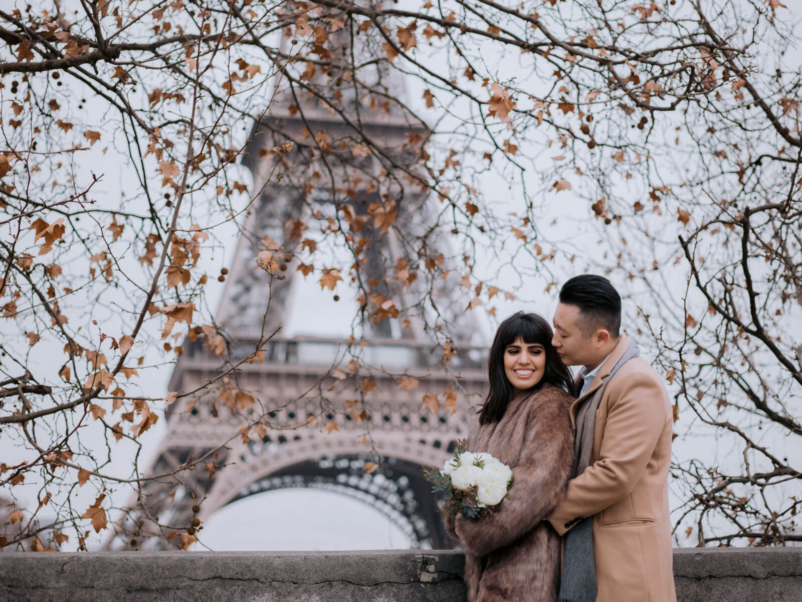The bride and groom is standing in front of the Eiffel Tower, Paris, France for their New Year's destination wedding. Image by Jenny Fu Studio