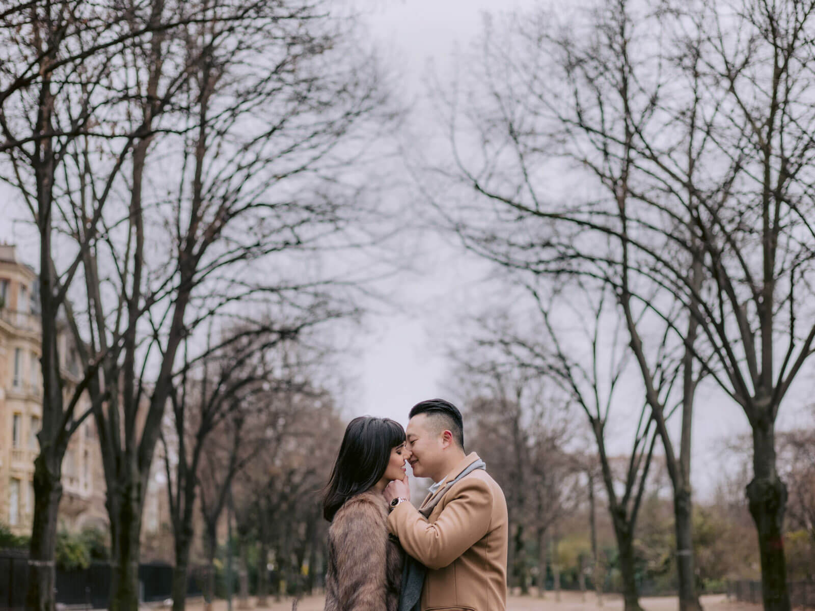 The bride and groom are about to kiss amidst dry trees in Paris, France for their New Year's destination wedding. Image by Jenny Fu Studio