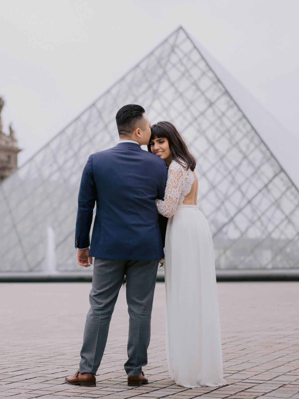 The groom is kissing his bride in the forehead, in Paris, France. Destination wedding image by Jenny Fu Studio