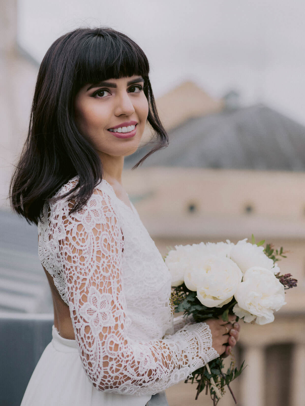 The pretty bride is smiling, holding her flower bouquet, in Paris, France. Image by Jenny Fu Studio
