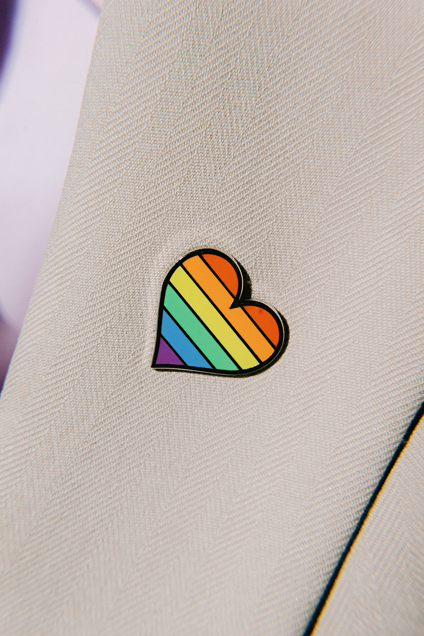 A rainbow-colored heart-shaped pin is on a groom's coat.