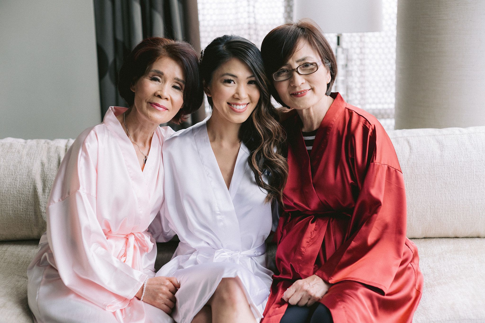 The bride is wearing her robe, while the two ladies with her are wearing red and pink robes. Love month wedding image by Jenny Fu Studio.