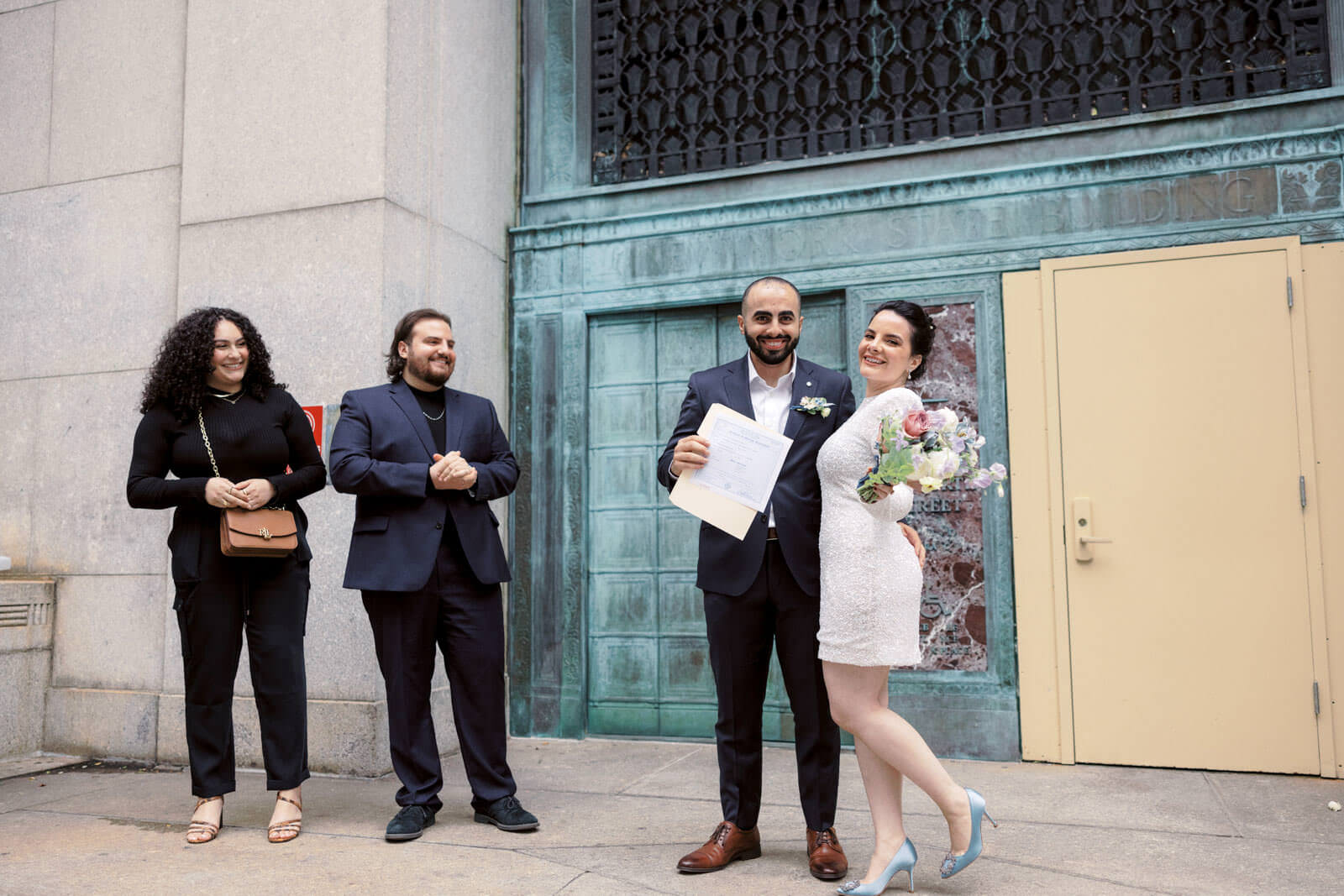 The bride, groom and two guests are outside the exit door after the ceremony. NY City Hall elopement image by Jenny Fu Studio.