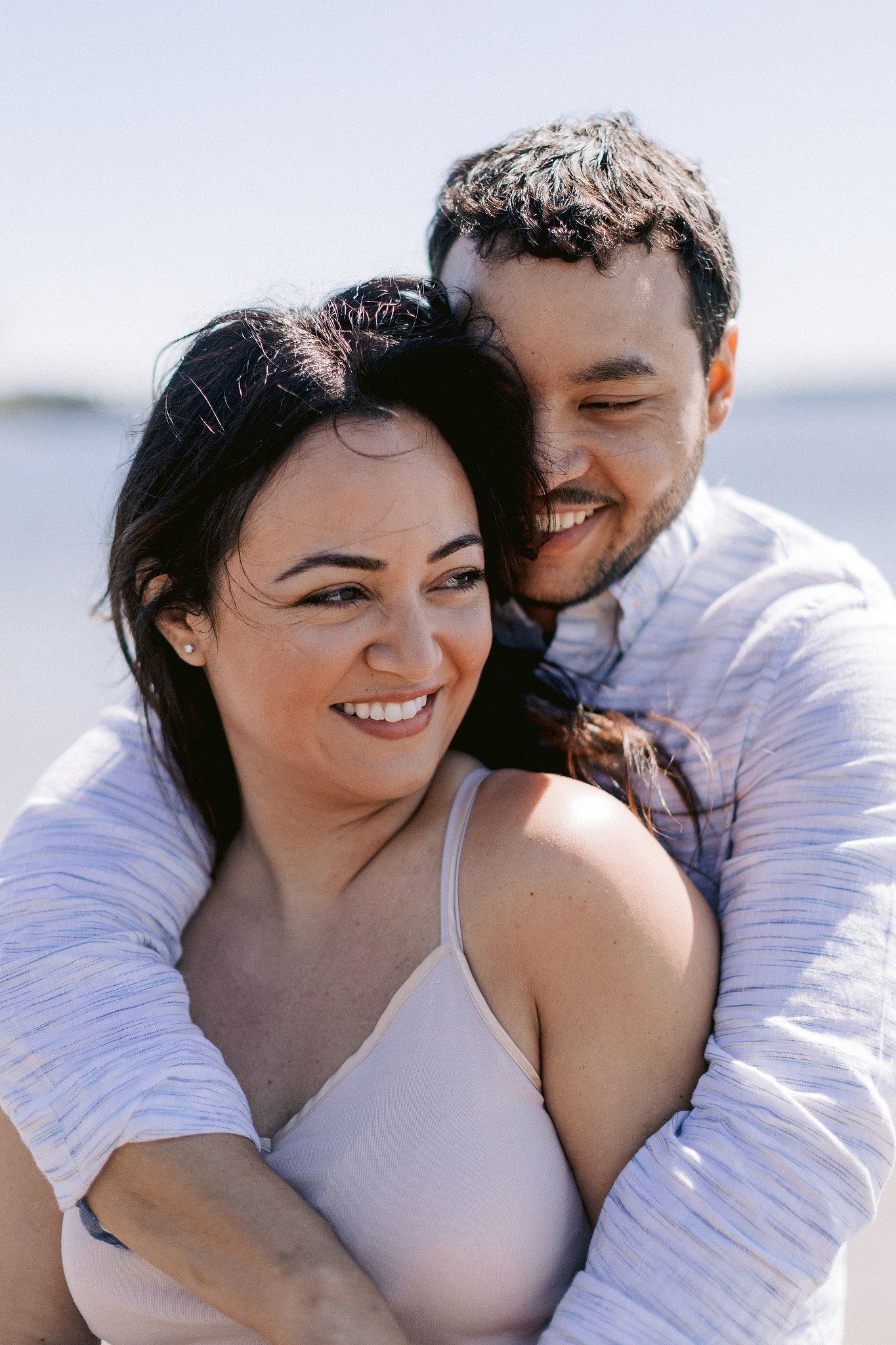 The man is hugging his soon-to-be wife in the seashore. NYC spring engagement Image by Jenny Fu Studio