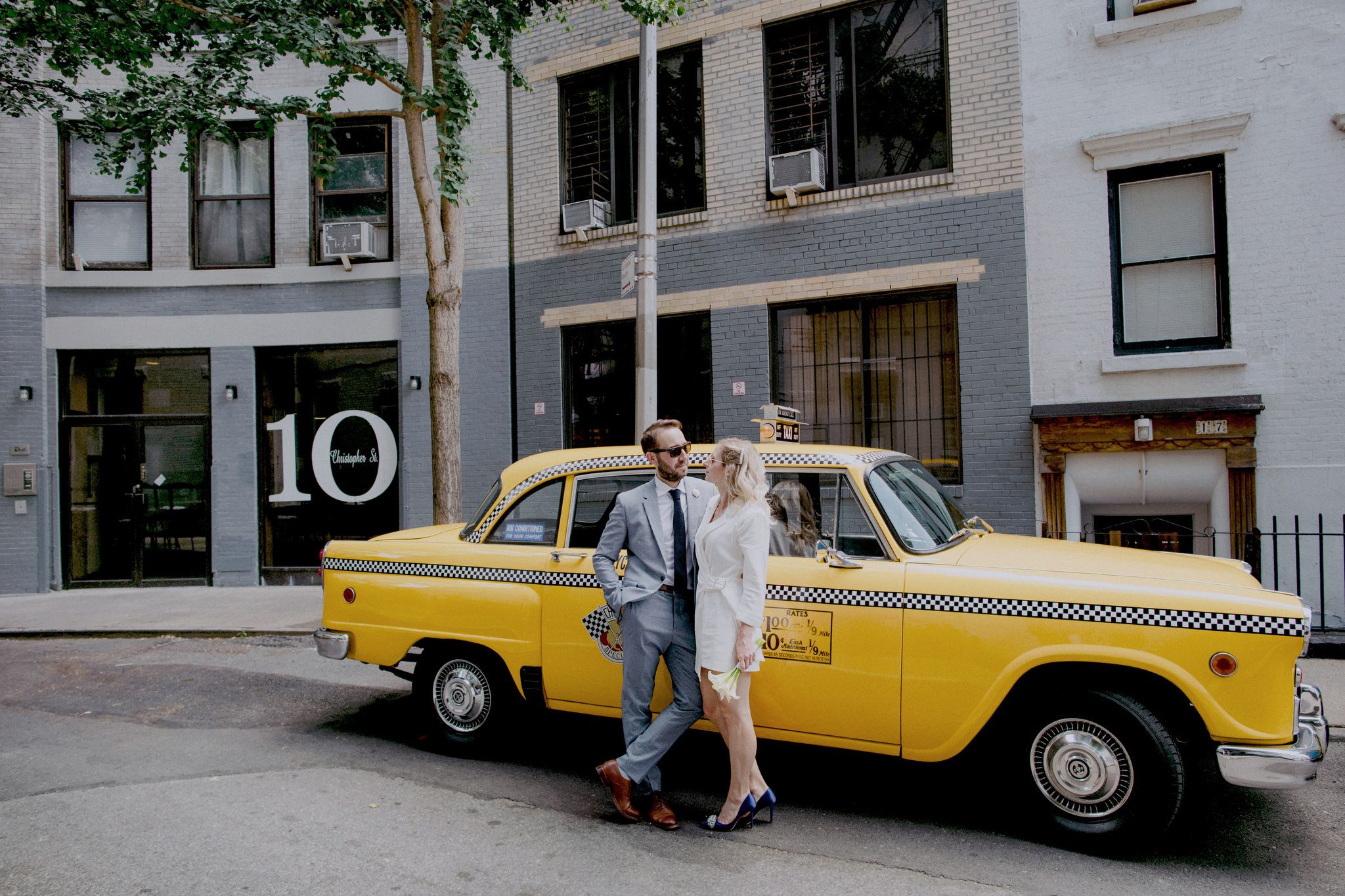 The bride and groom are chatting beside a classic NYC checkered yellow cab