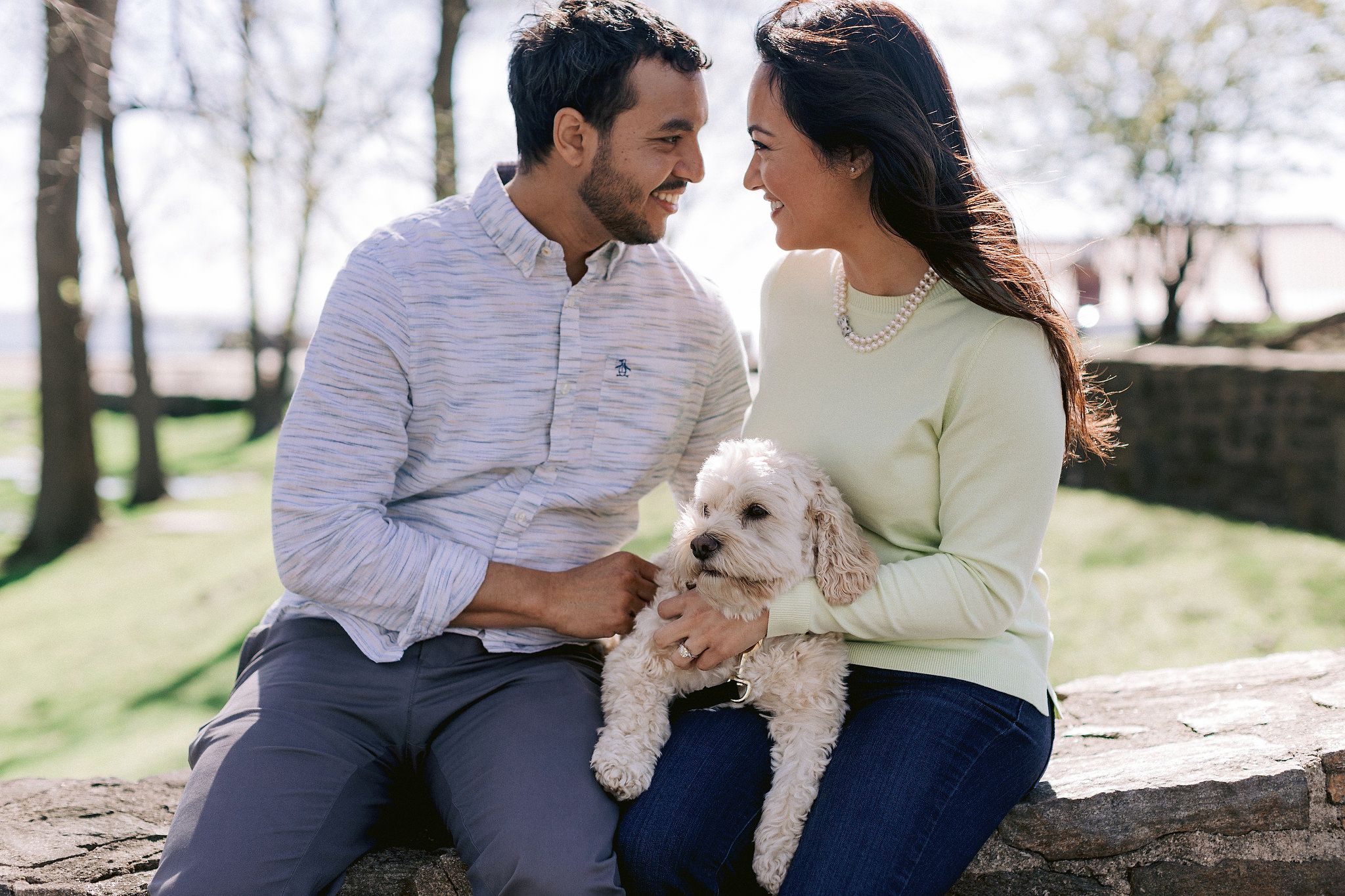 The couple are happily looking at each other while holding their dog. NYC spring engagement Image by Jenny Fu Studio