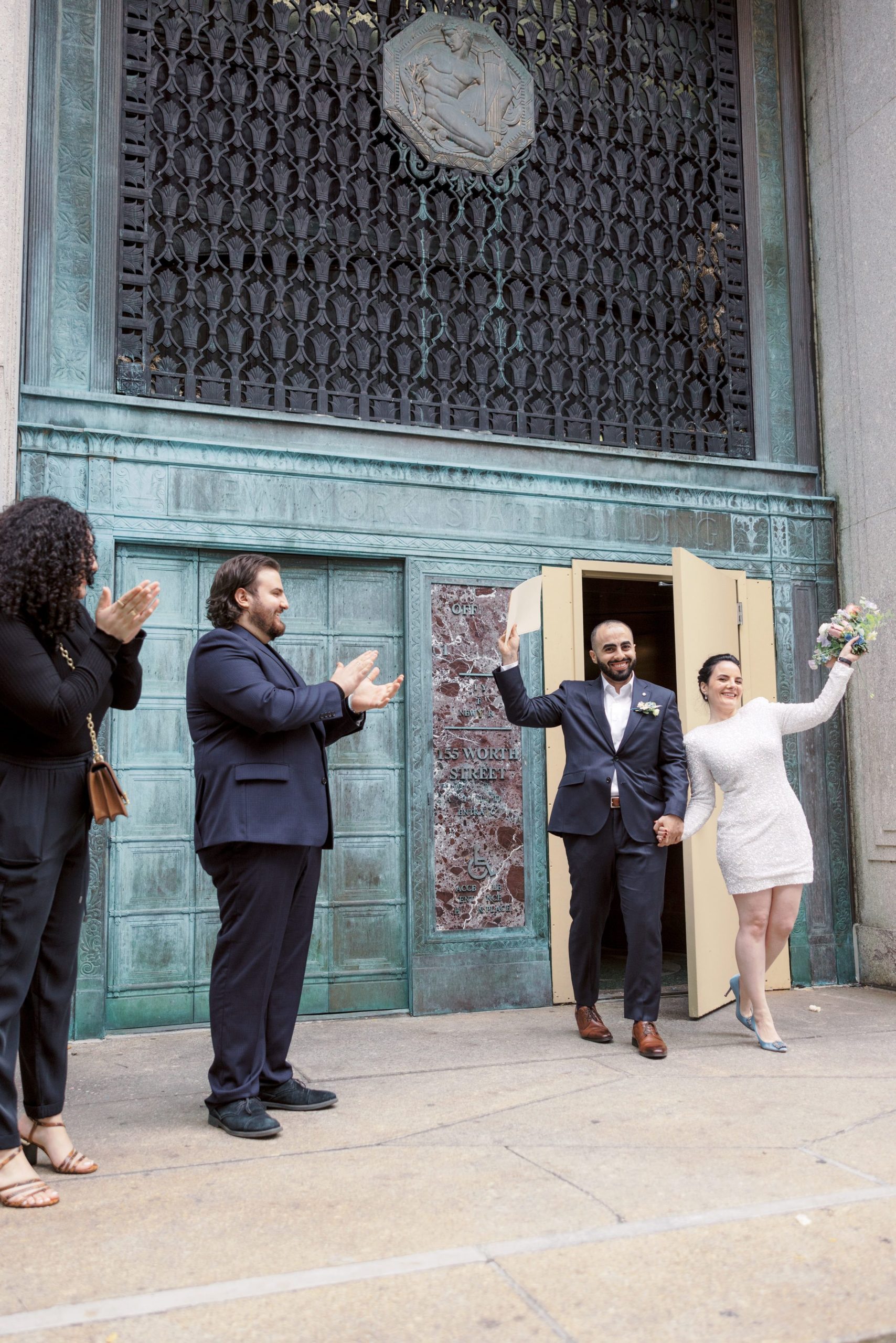 The bride and groom happily exited the NYC City Hall as their guests cheer on. Elopement image by Jenny Fu Studio