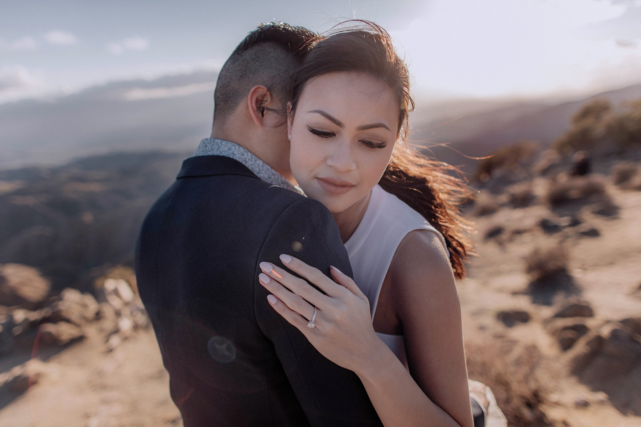 The engaged couple are hugging each other with mountains in the background. Spring engagement session outfit image by Jenny Fu Studio