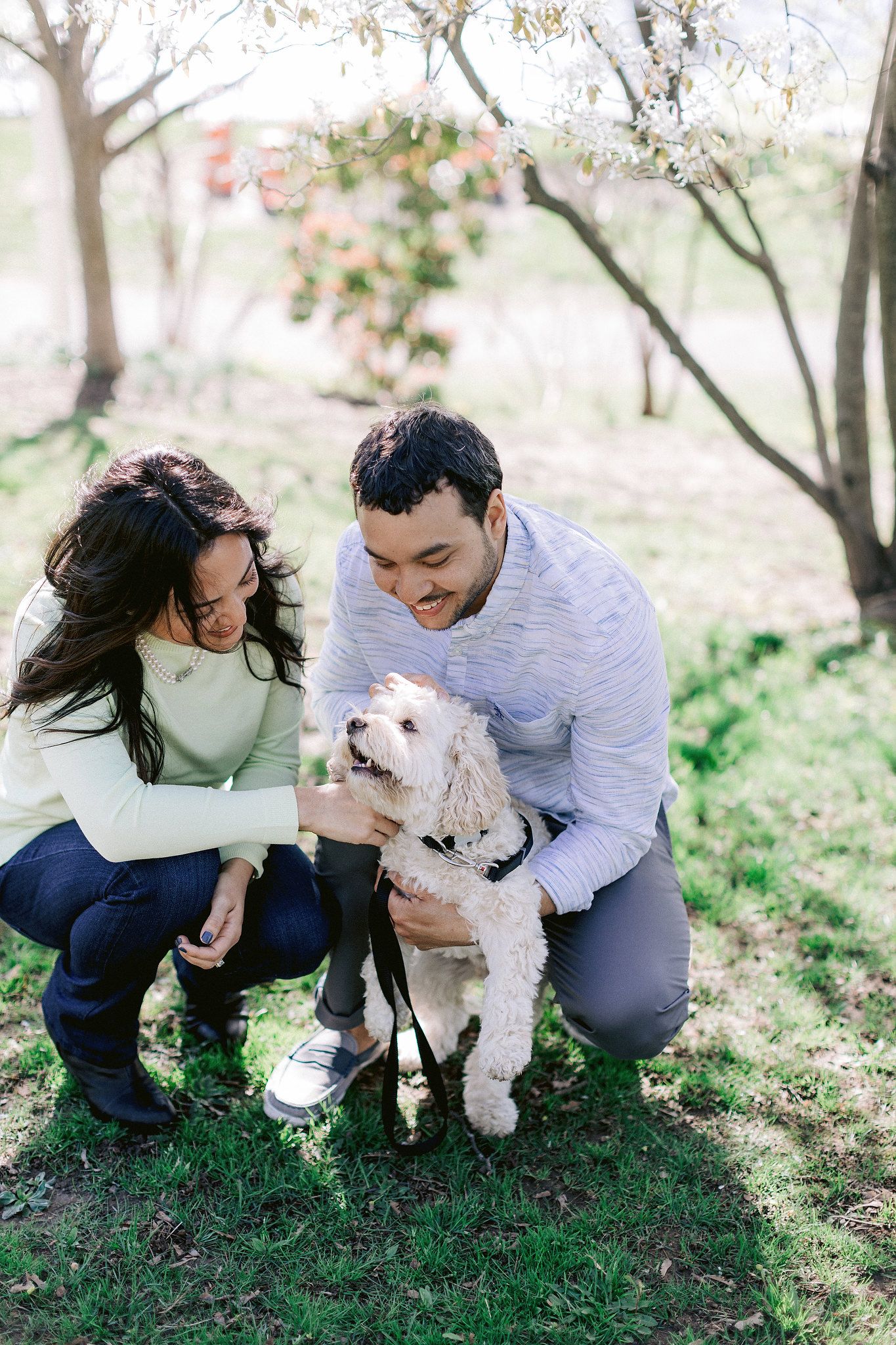 The couple are happily patting their dog in a garden. NYC spring engagement Image by Jenny Fu Studio