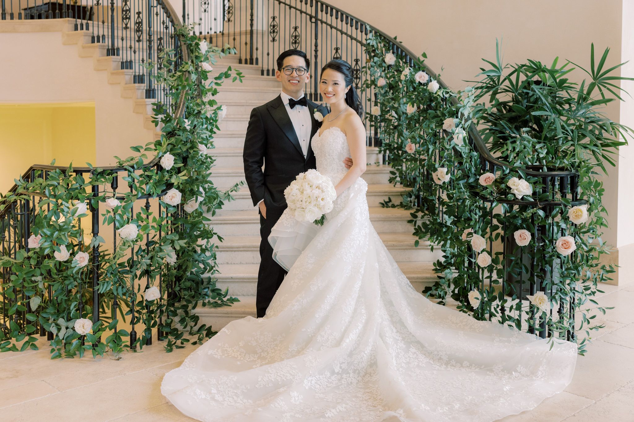 The bride and the groom are standing on the bottom of the staircase, which is filled with many vines and white flowers. Image by Jenny Fu Studio