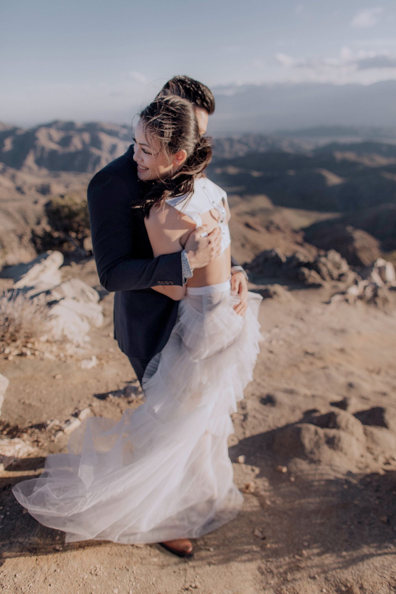 The engaged couple are hugging each other with mountains in the background. Spring engagement session outfit ideas. Image by Jenny Fu