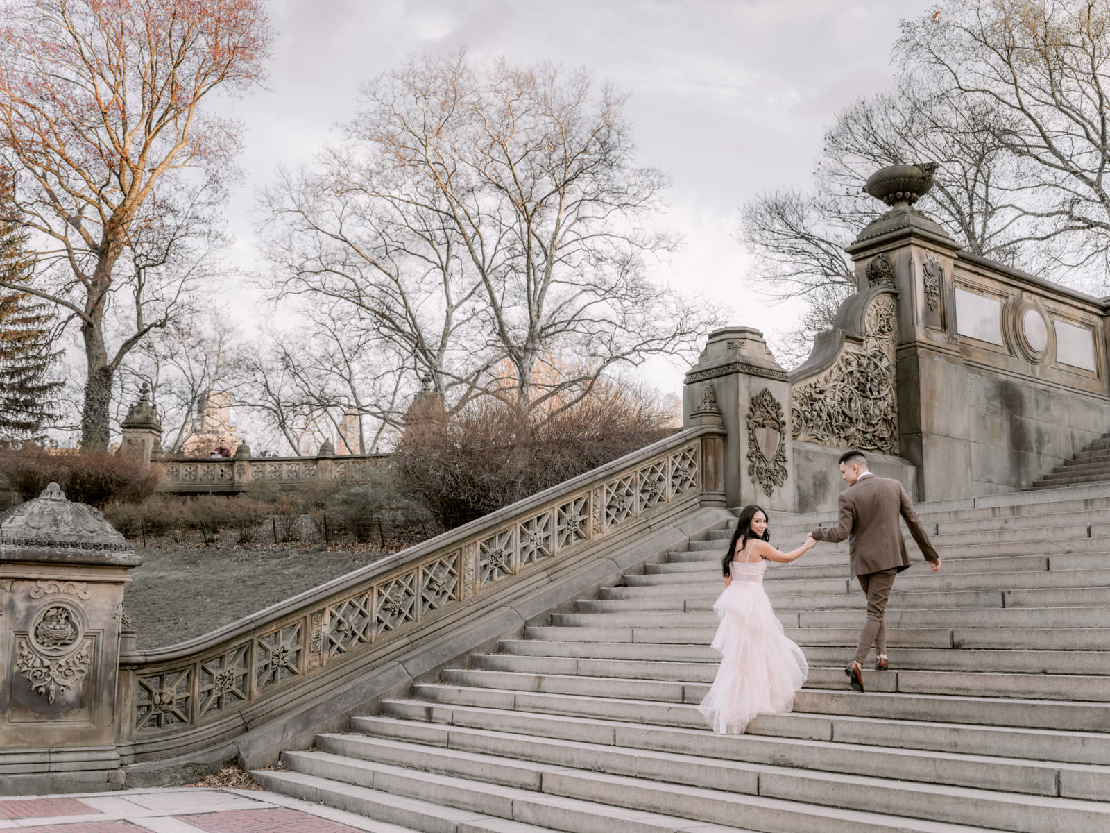 The engaged couple are climbing up a staircase at Central Park, New York City. Bridgerton inspired Editorial engagement session by Jenny Fu Studio