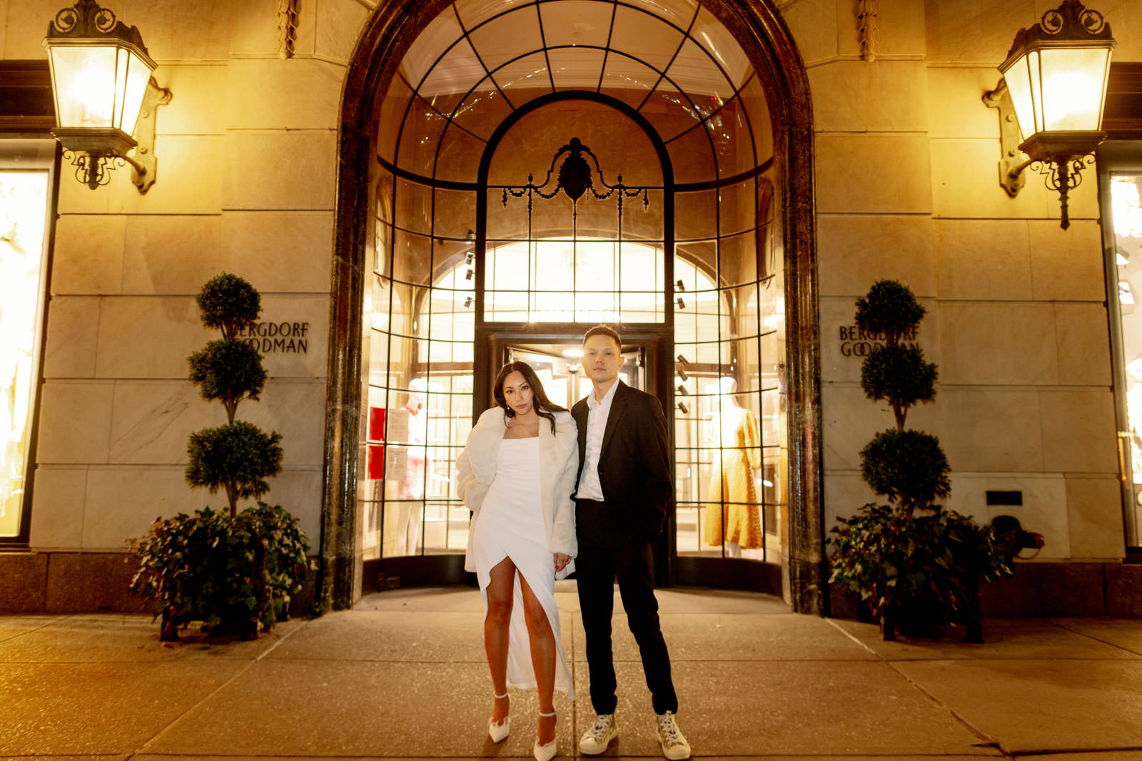 The chic and stylish engaged couple is standing in front of Berdorf Goodman, New York City. Editorial winter engagement photo by Jenny Fu Studio