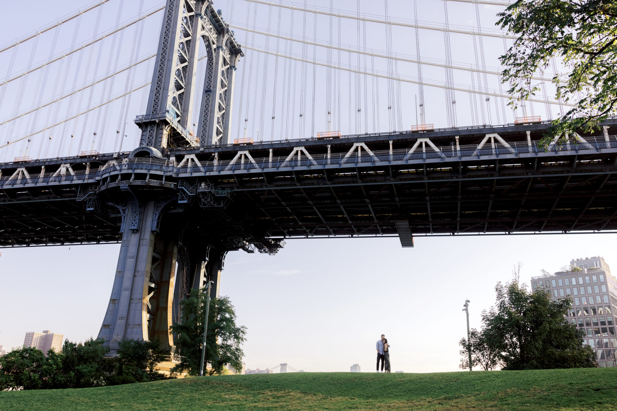 The couple are standing underneath the Brooklyn Bridge. Image by professional engagement photographer Jenny Fu