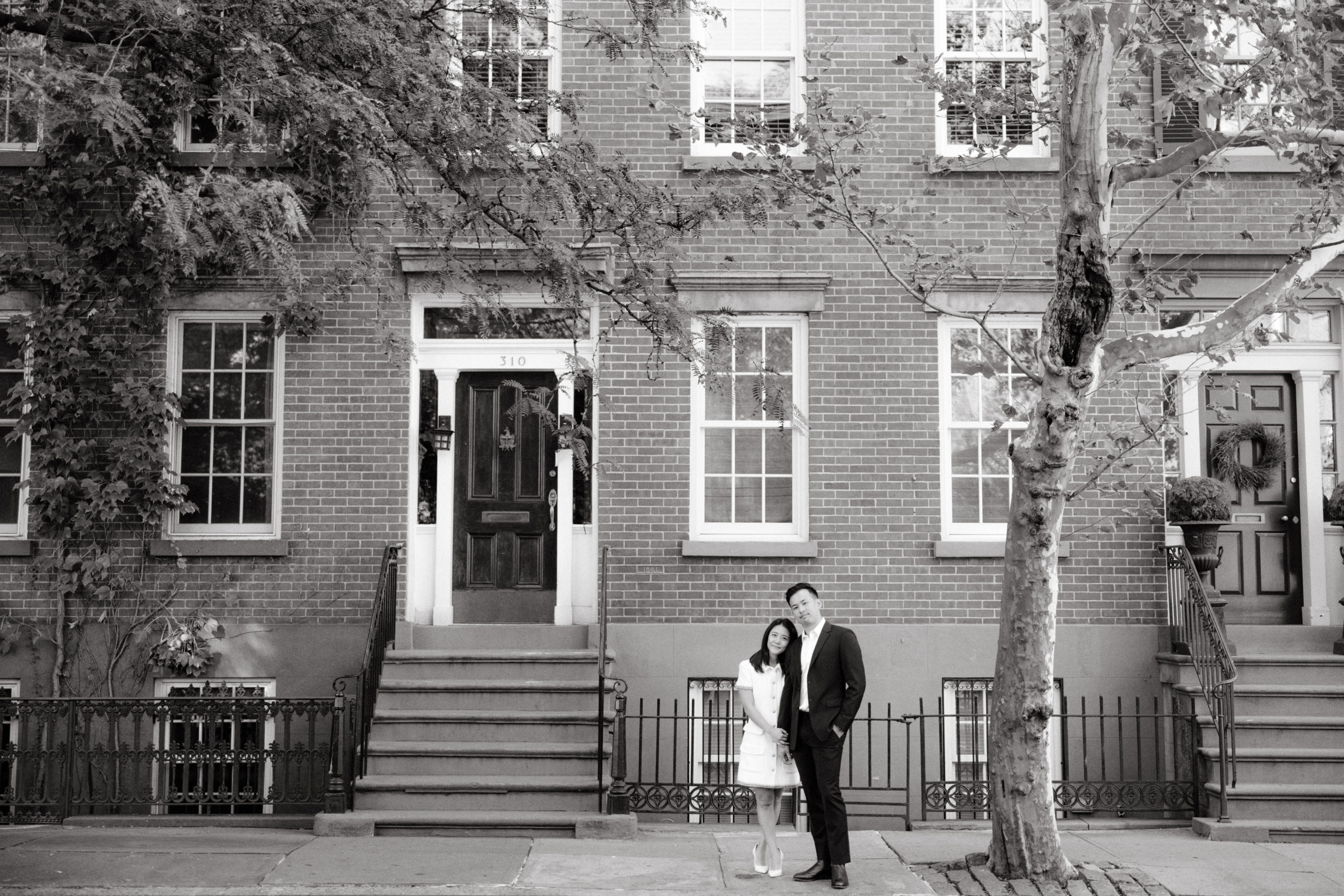 Black and white photo of the engaged couple in front of the houses in West Village, New York. Editorial engagement image by Jenny Fu Studio