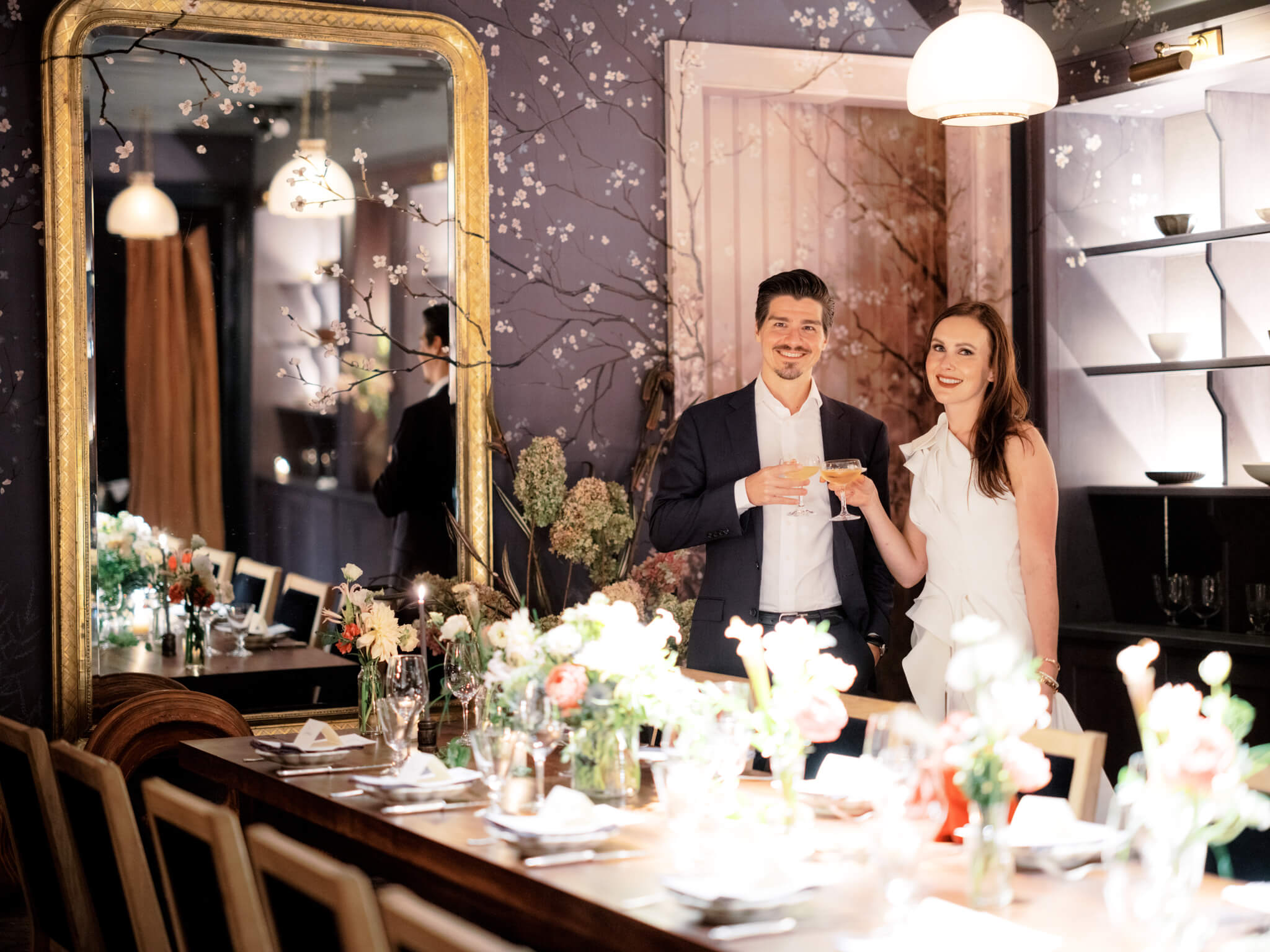 The bride and groom are holding champagne glasses inside a wedding reception room at La Mercerie Soho Hotel for their intimate wedding. Image by Jenny Fu Studio