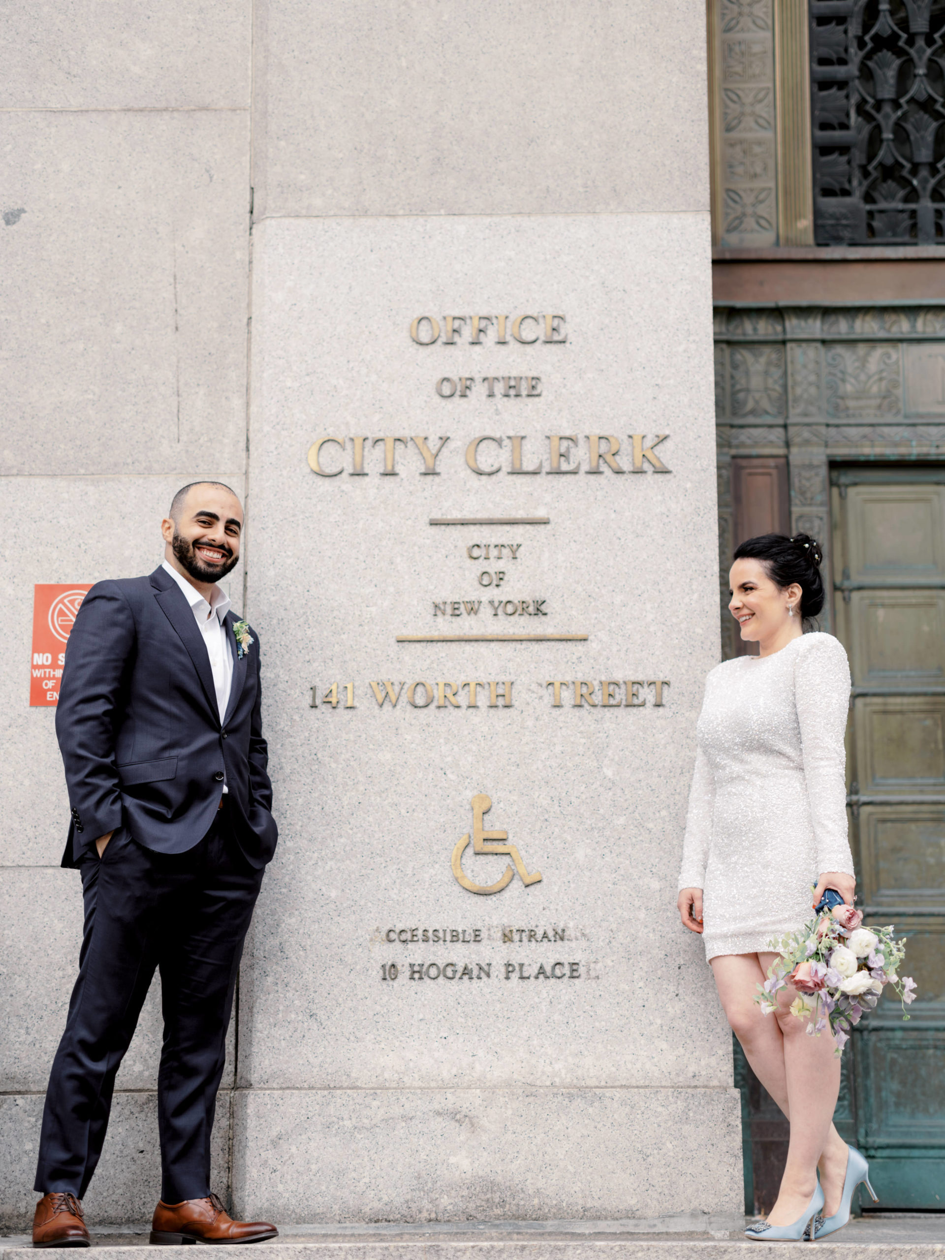 The bride and groom are in front of the Office of the City Clerk at 141 Worth Street New York for their city hall elopement. 