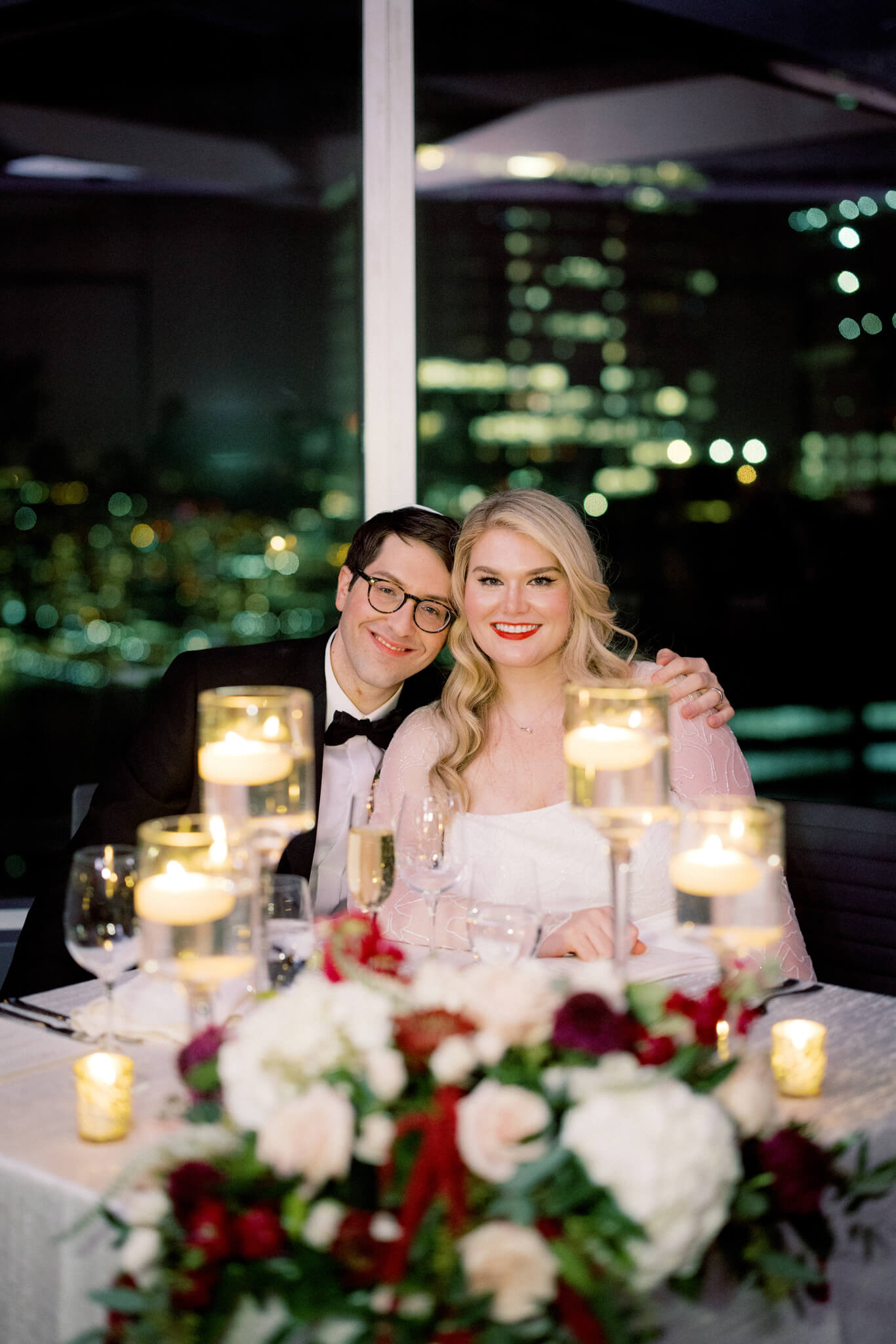 Image of the smiling bride and groom while sitting on their reception table at Manhatta Restaurant. Image by Jenny Fu Studio