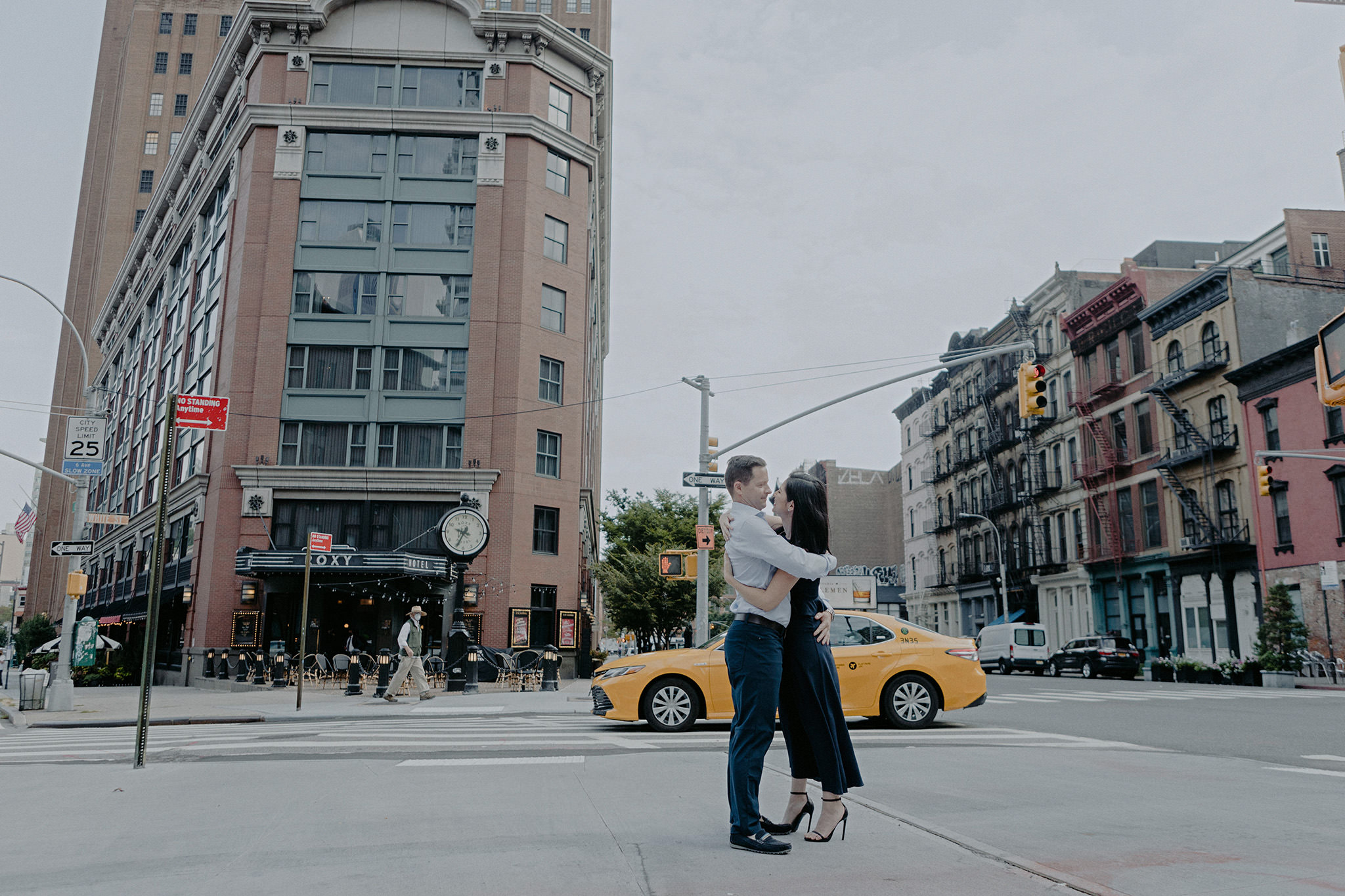 The engaged couple is hugging each other in New York City, with a yellow cab ad buildings in the background. Editorial image by Jenny Fu Studio