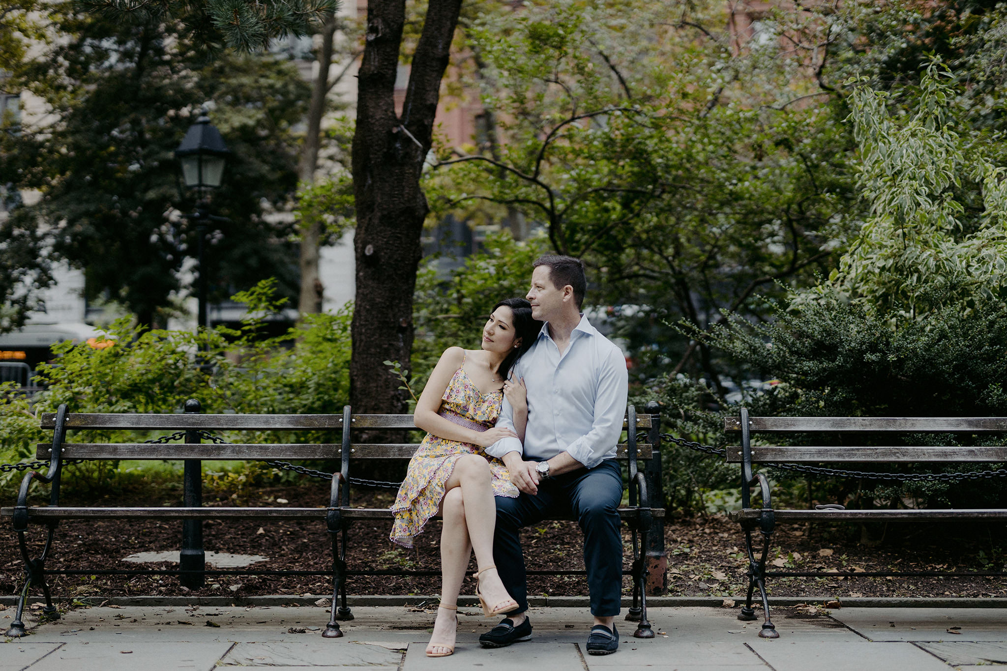 The engaged couple is romantically sitting in a bench at Central Park. Editorial summer NYC engagement image by Jenny Fu Studio