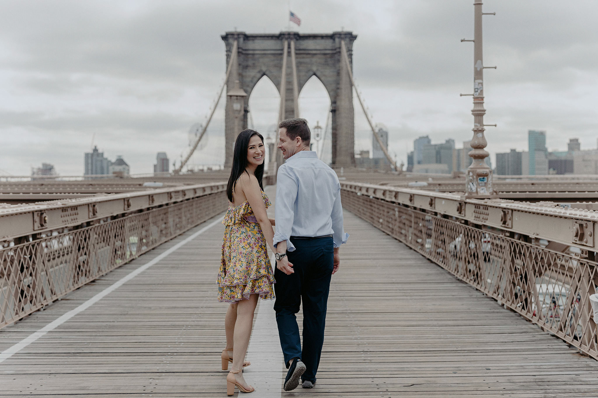 Back view of the couple happily walking in Brooklyn Bridge. Editorial NYC summer engagement photo by Jenny Fu Studio