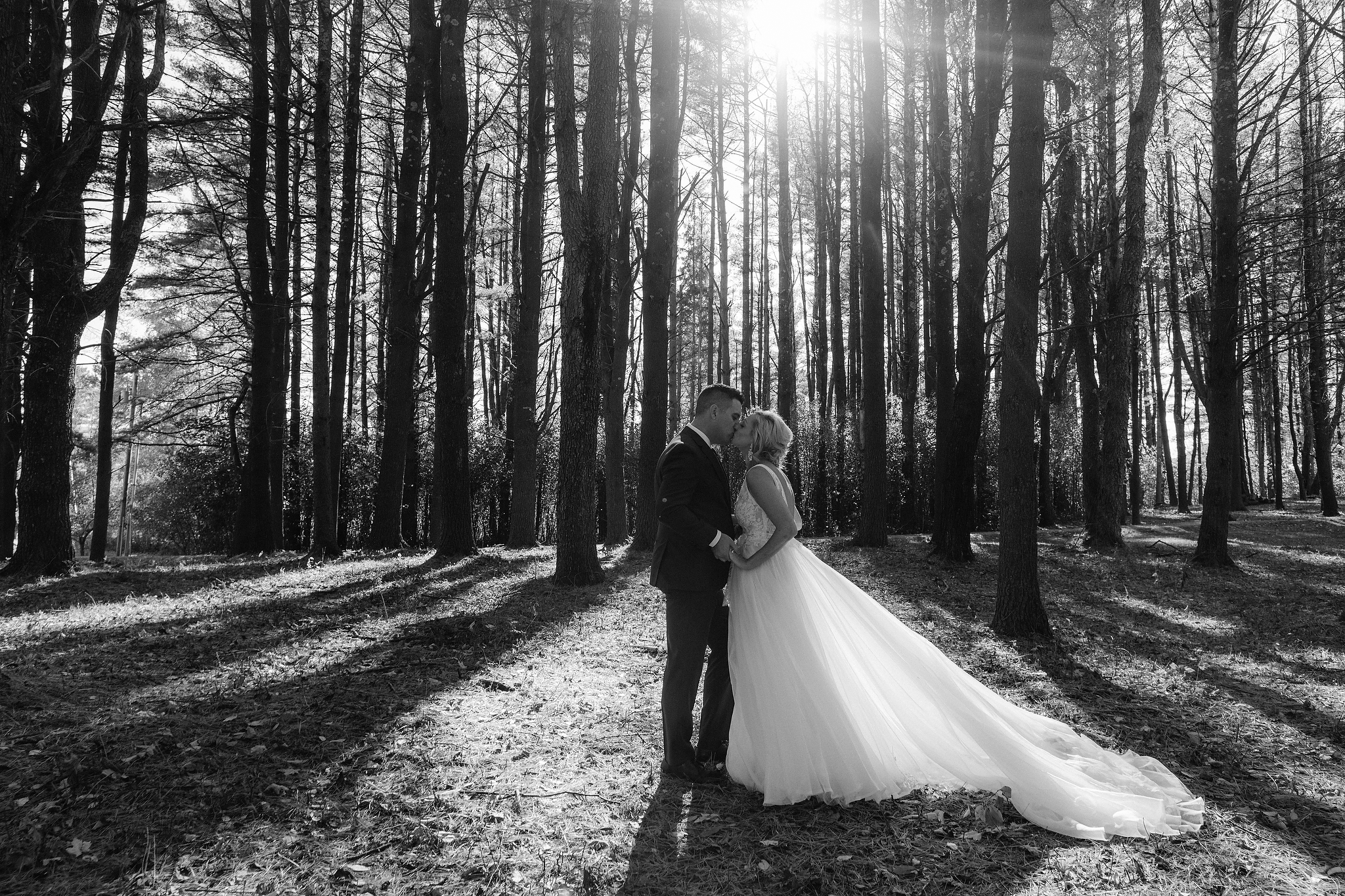 Black and white photo of the bride and groom kissing each other with many tall trees in the background. Editorial destination wedding image by Jenny Fu Studio. 