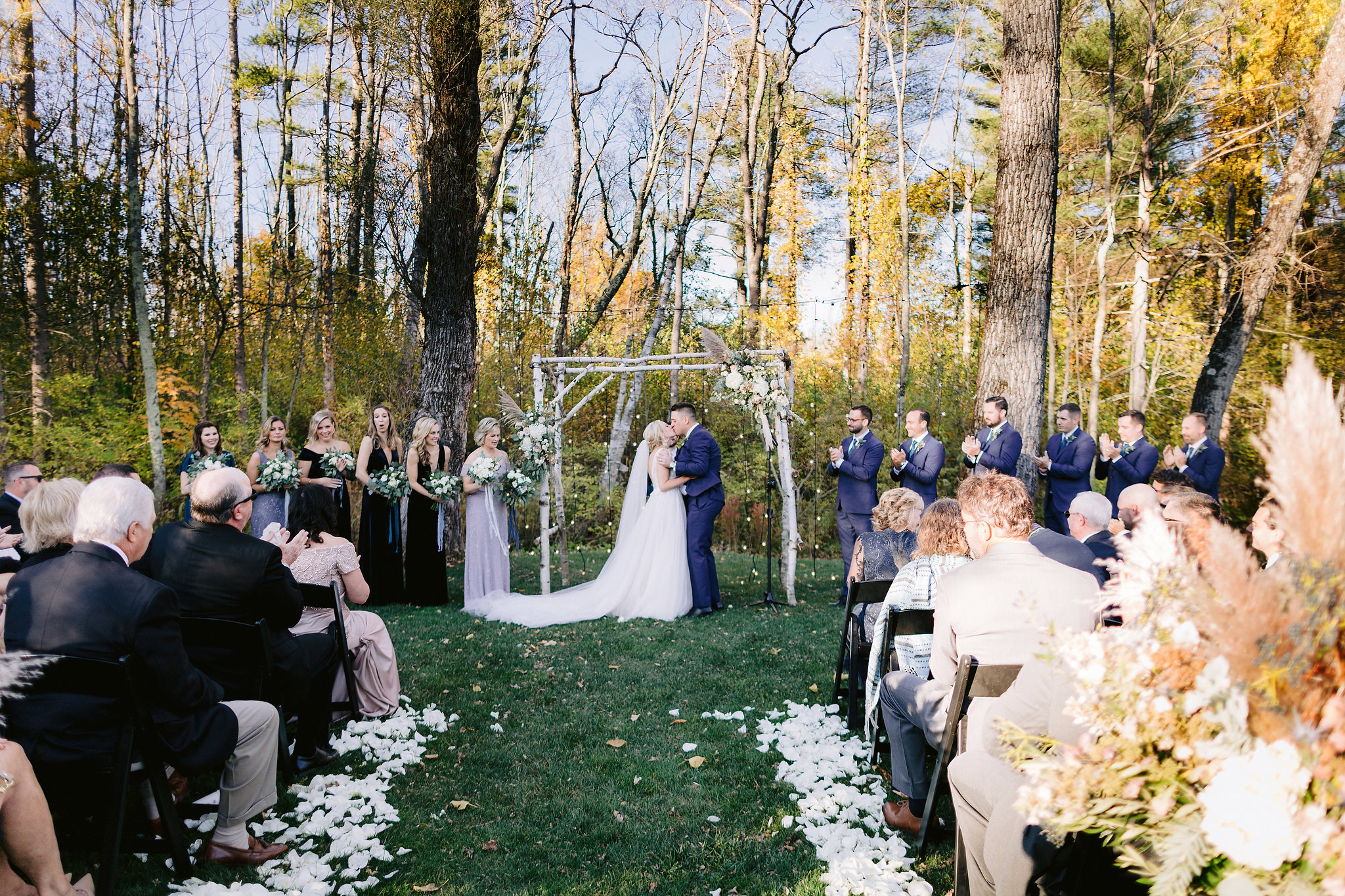 The bride and groom are kissing each other under their wedding arch as the ceremony ended while the guests are watching.