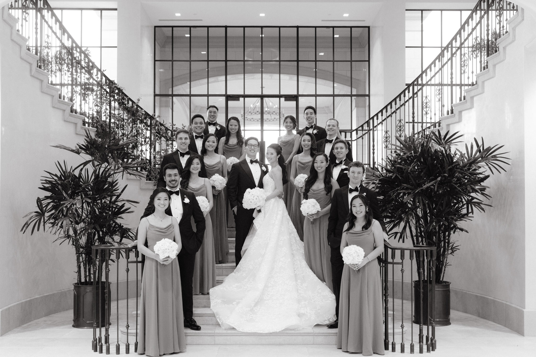 The bride, groom, bridesmaids and groomsmen are standing on the grand staircase. NYC wedding venue image by Jenny Fu Studio