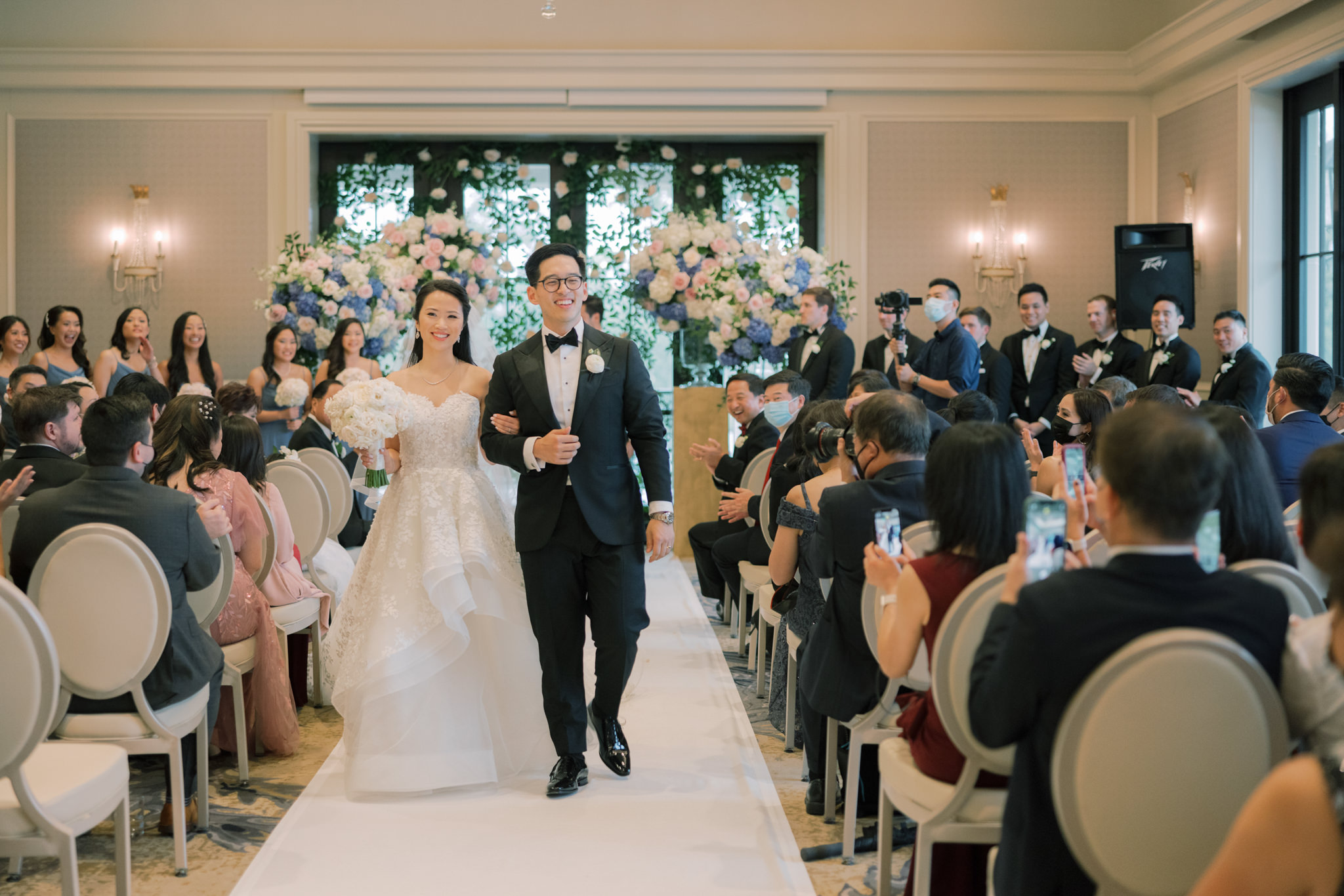 The bride and groom are happily walking away from the aisle as the guests cheer on. Image by Jenny Fu Studio