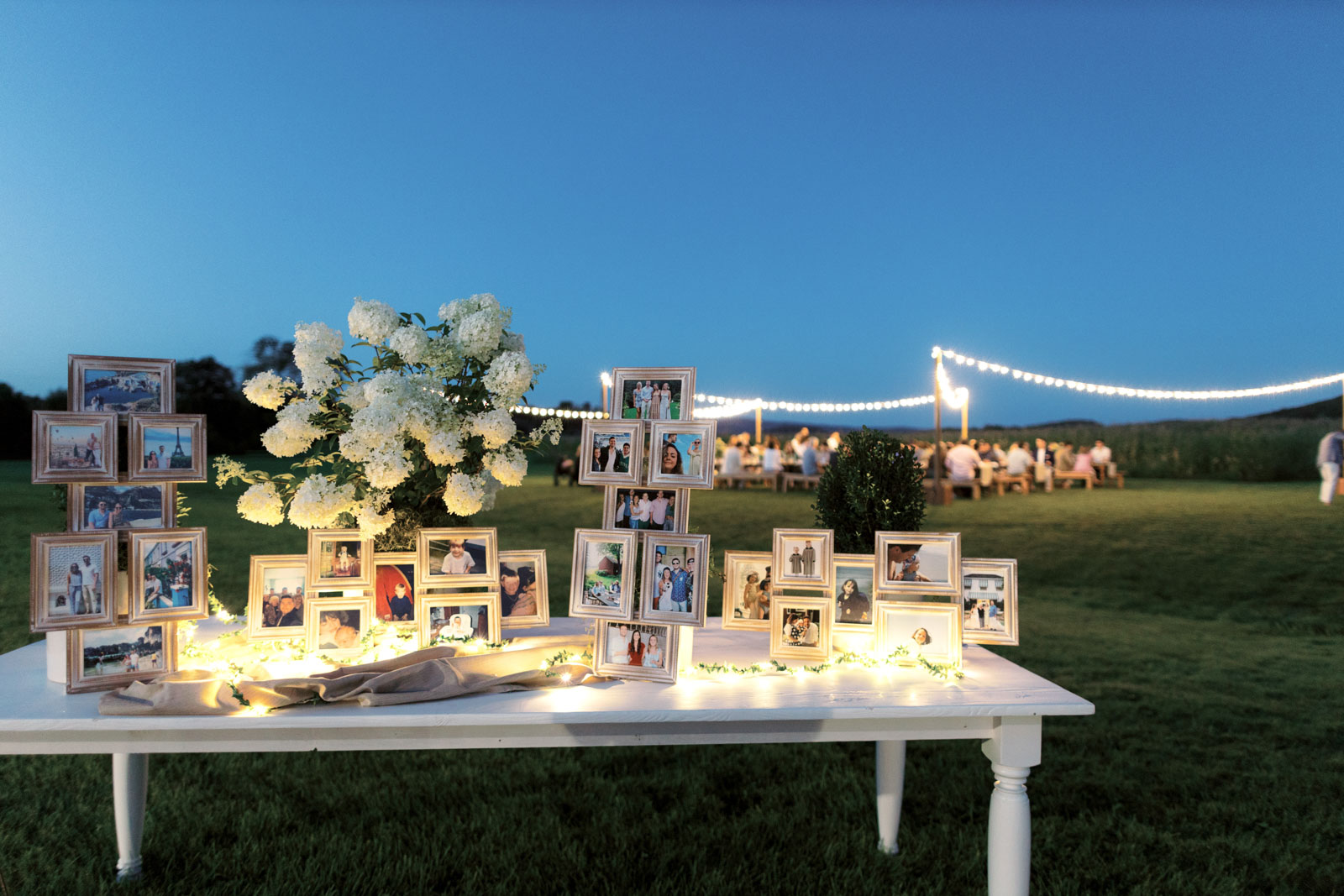 A table is filled with framed photos, flowers, and fairy lights for a rehearsal dinner. Editorial image by Jenny Fu Studio