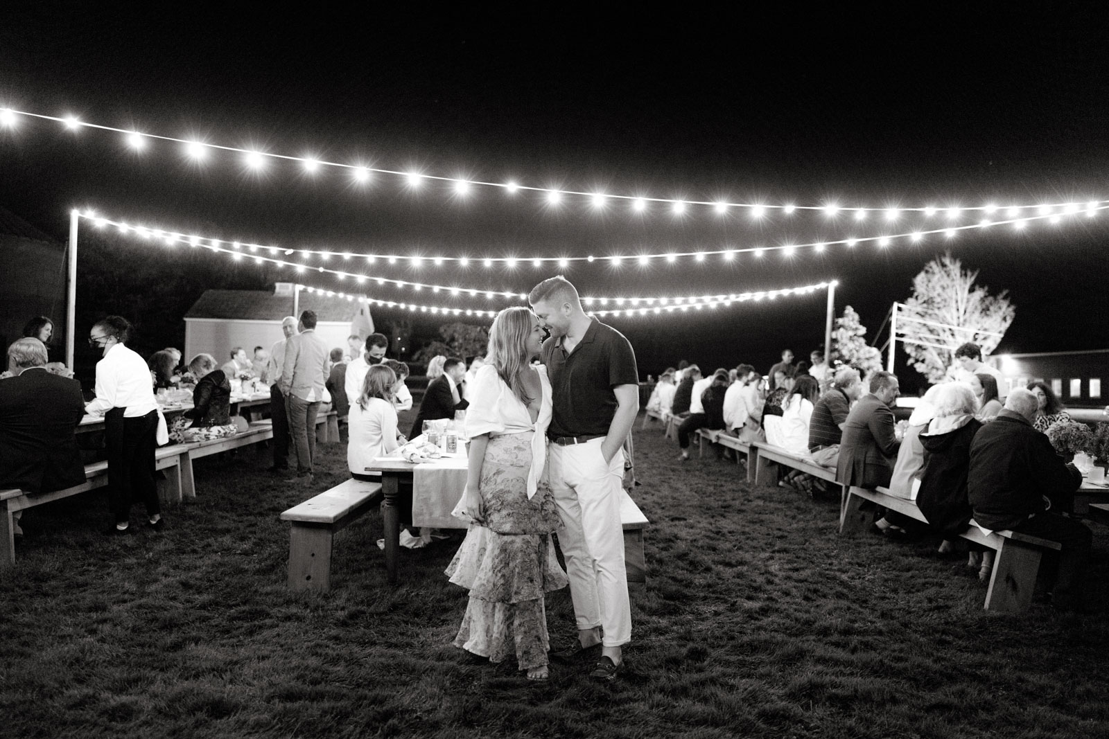 Black and white image of the bride and groom happily standing close to each other in front of their guests. Editorial rehearsal dinner image by Jenny Fu Studio. 