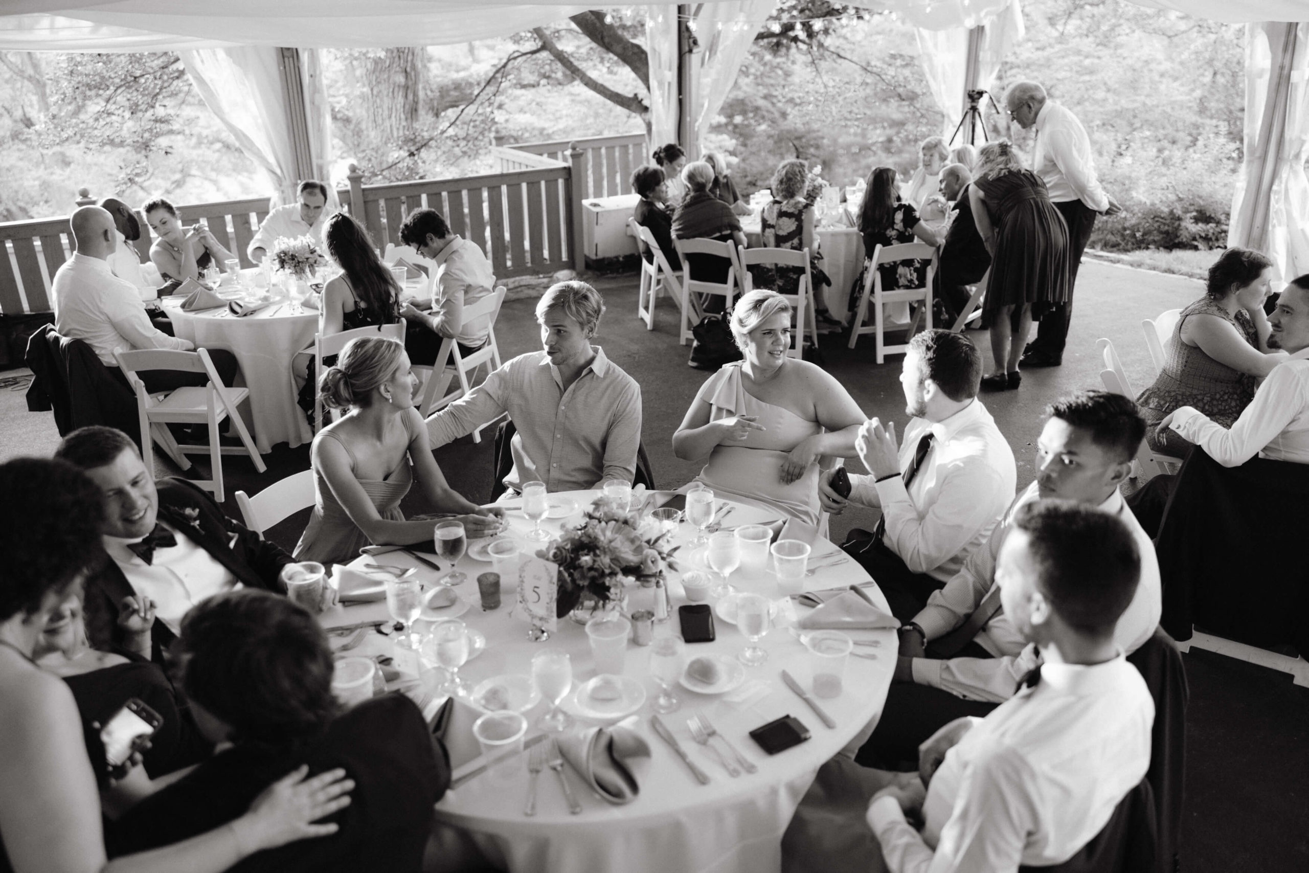 Black and white photo of the wedding guests seated on round tables chatting with each other. Destination wedding image by Jenny Fu Studio 