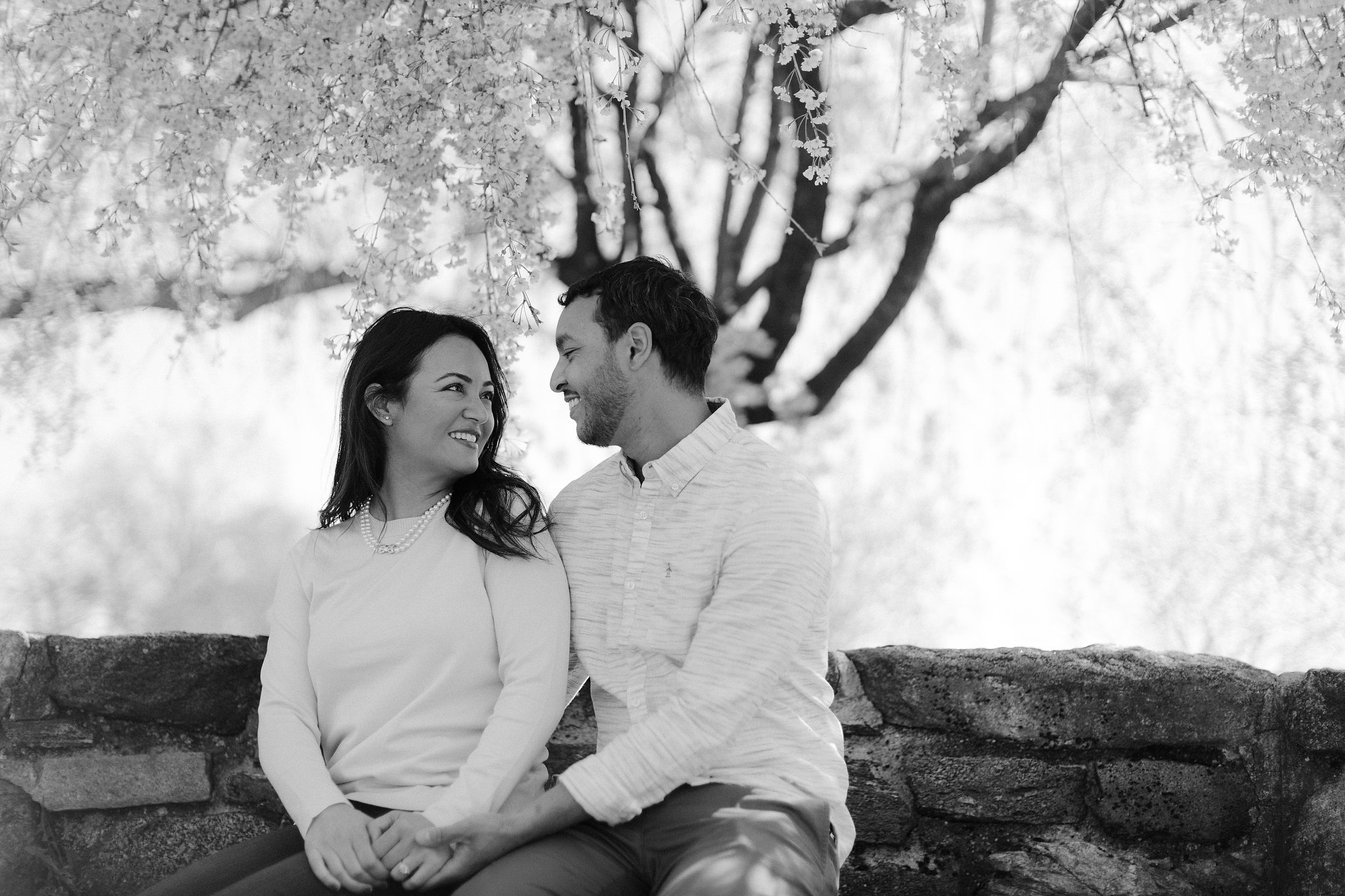 Black and white editorial photo of an engaged couple looking at each other while sitting in a park in NY. Image by Jenny Fu Studio