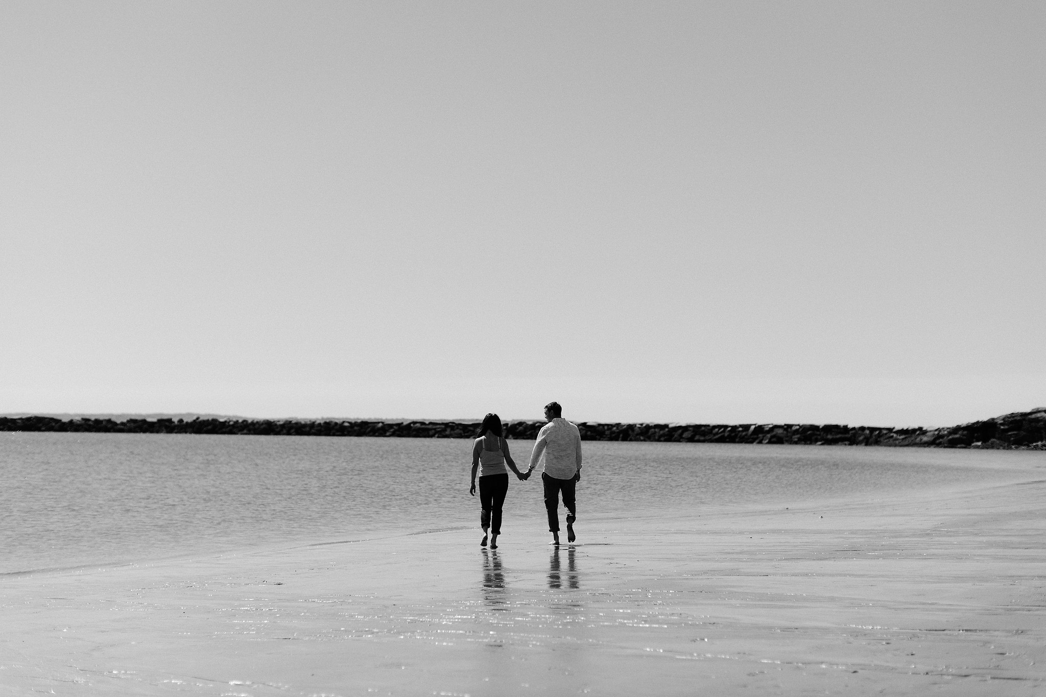 The engaged couple is holding hands while walking along the seashore. Editorial image by Jenny Fu Studio