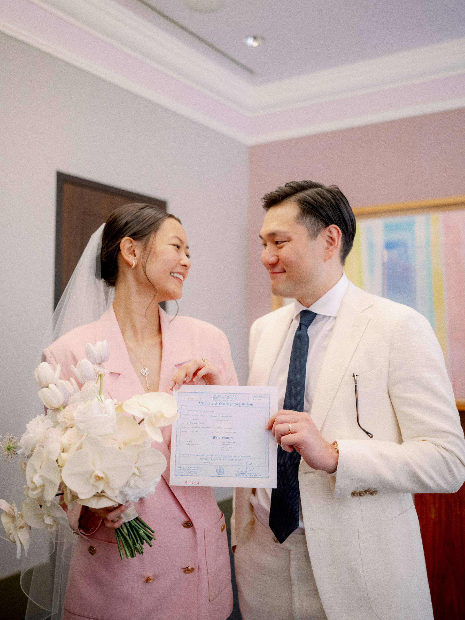 The bride and groom are holding their marriage certificate after the wedding ceremony at NYC City Hall. Editorial elopement image by Jenny Fu Studio.